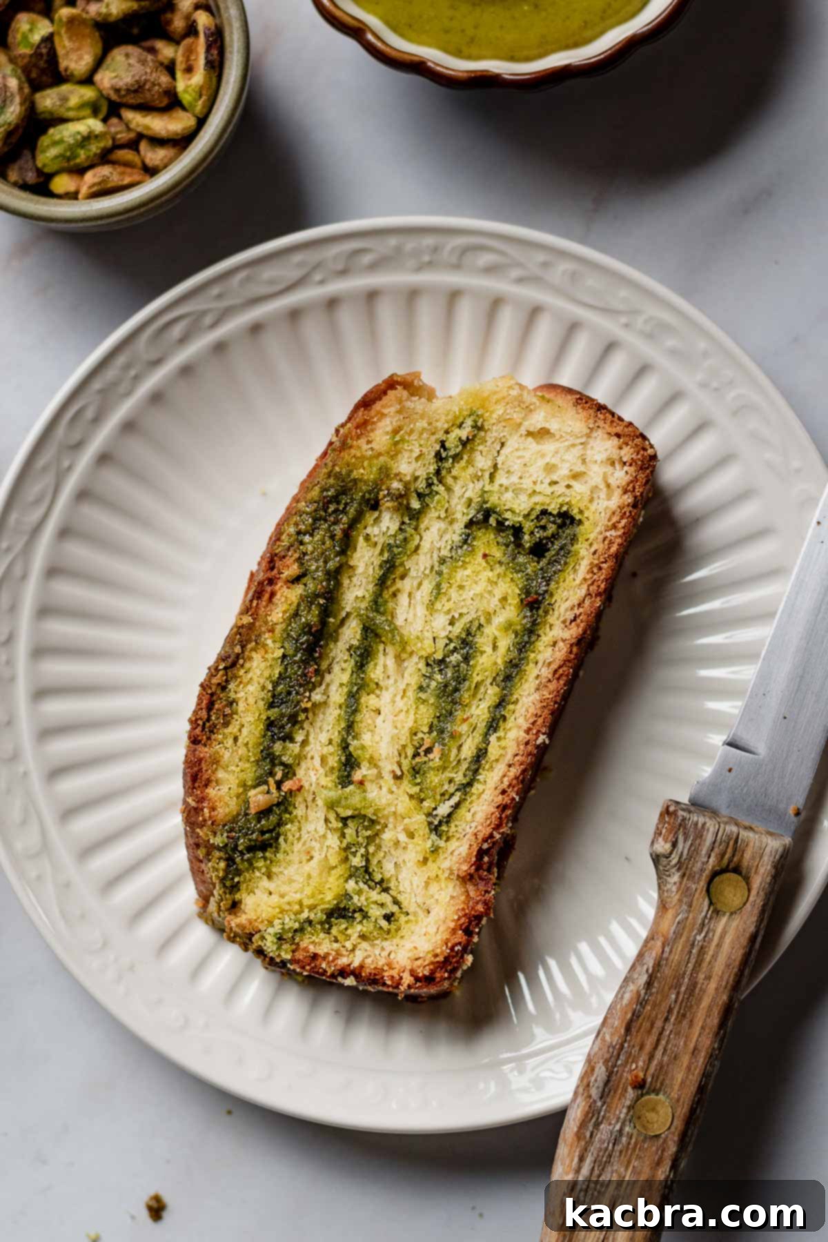 A single slice of fluffy pistachio babka, showcasing its intricate green and golden swirls, resting elegantly on a pristine white plate.