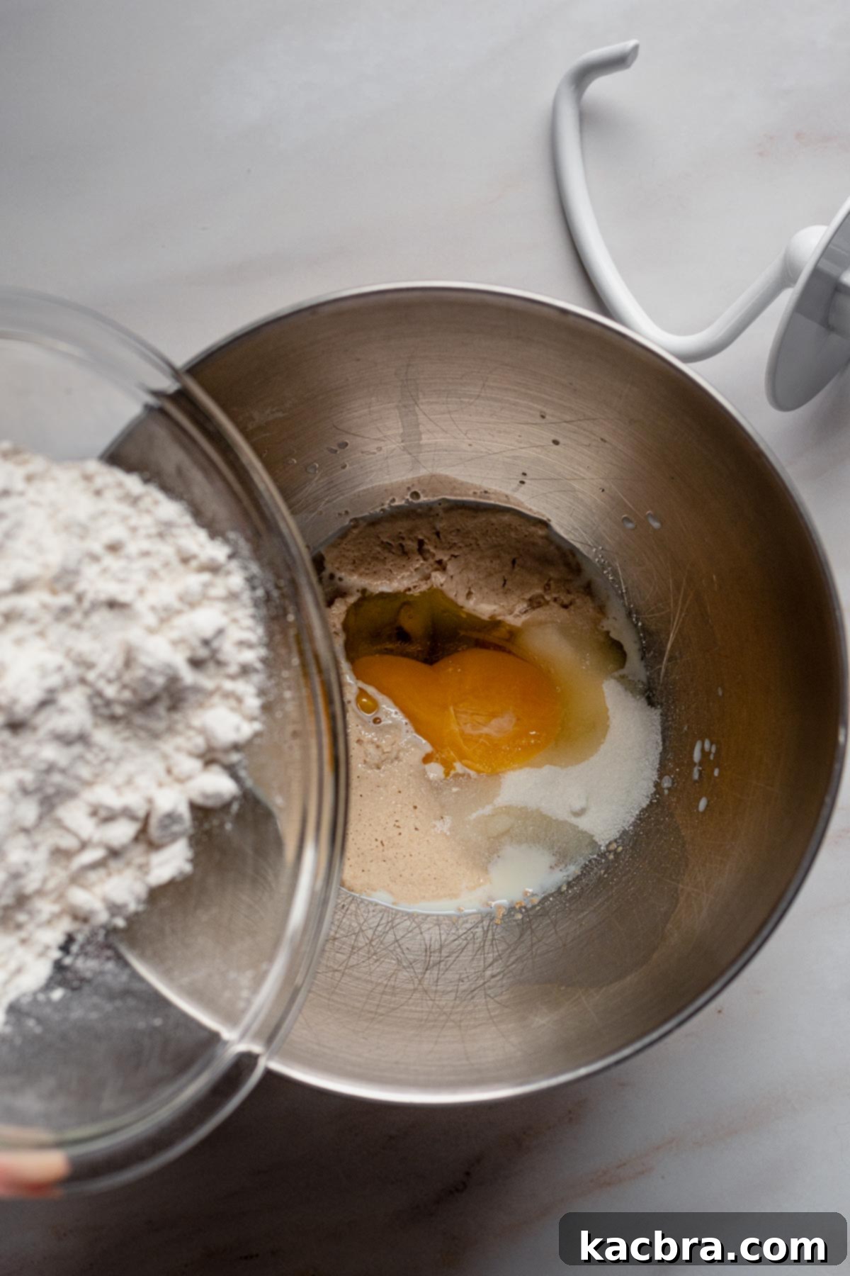 Dry ingredients like flour, salt, and the remaining sugar, along with eggs, added to the stand mixer bowl with activated yeast mixture.