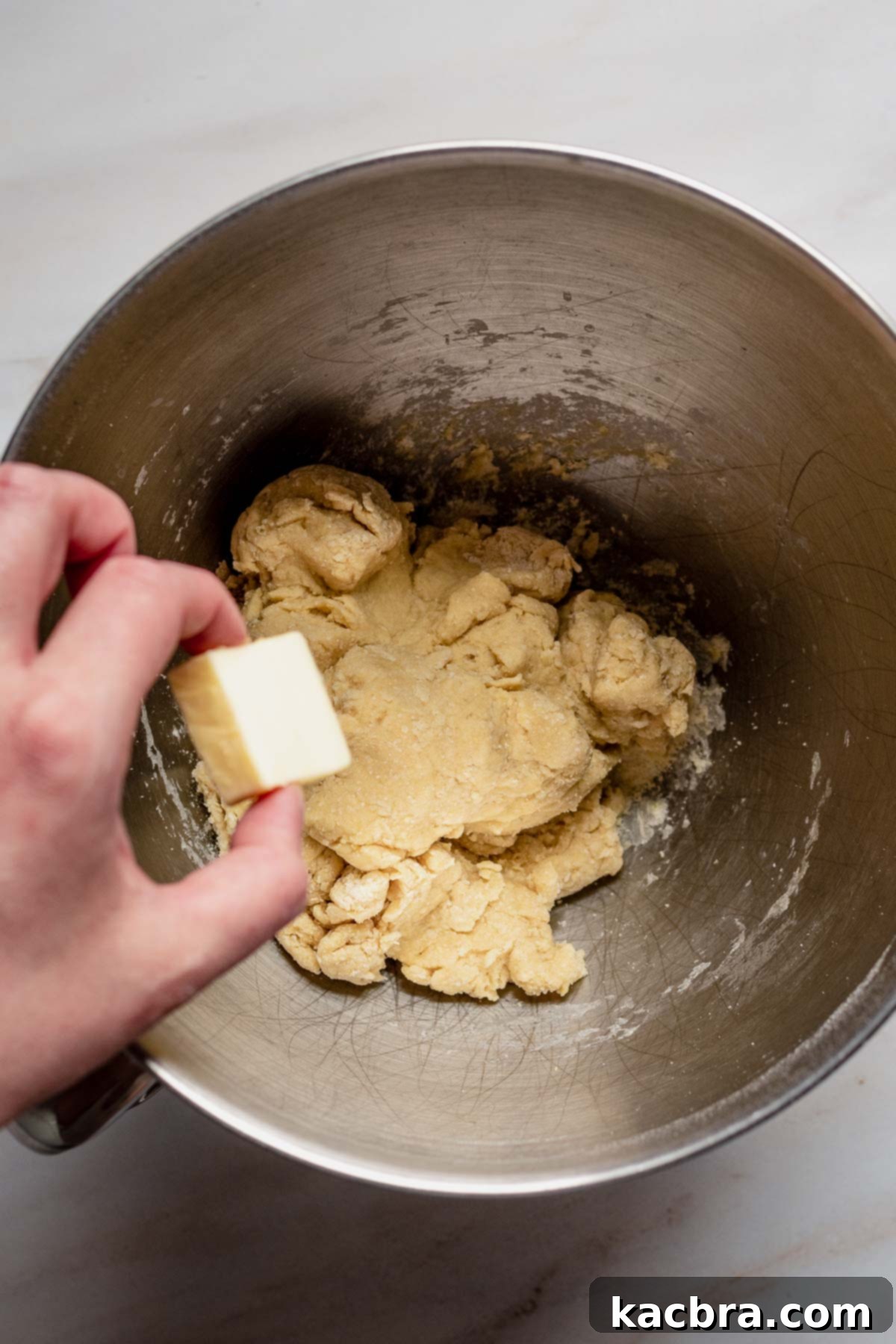 Softened butter cubes being gradually added to the developing babka dough in a stand mixer, ensuring thorough incorporation.