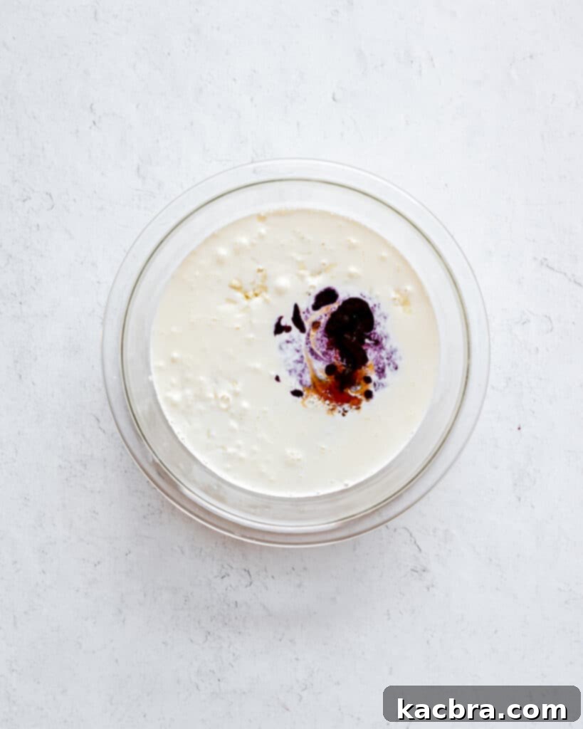 Hot cream poured over white chocolate and blueberry puree in a bowl, resting.