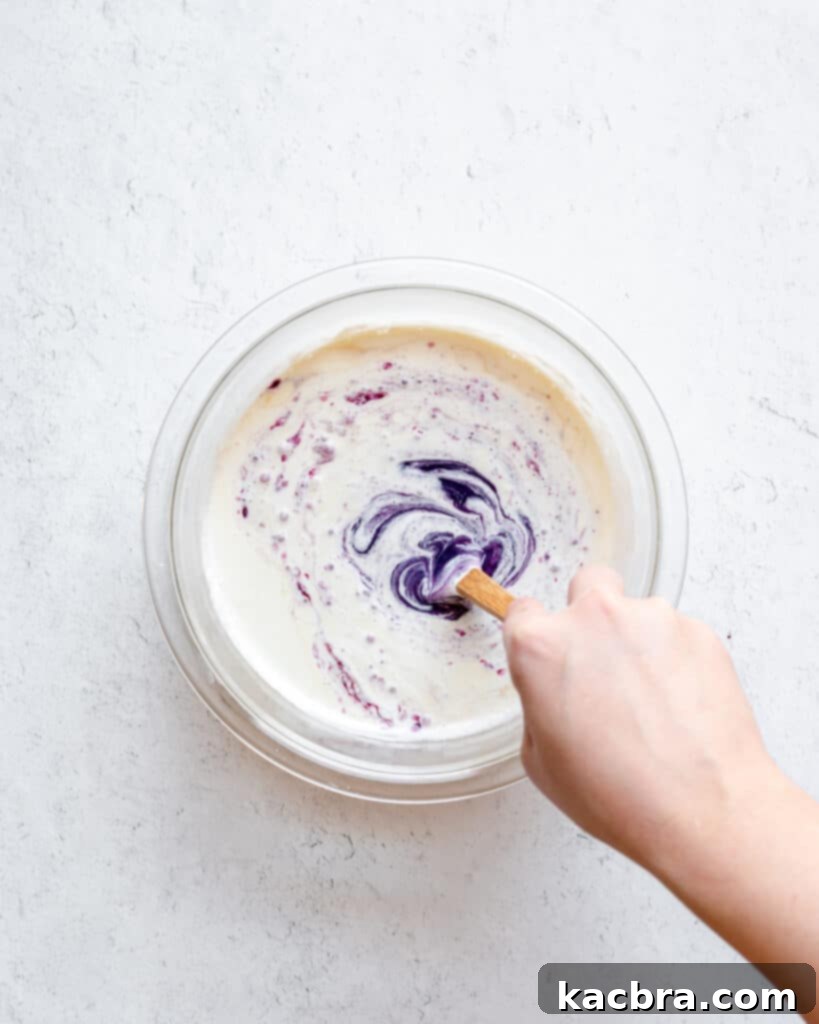 The process of stirring the blueberry ganache, showing the purple color emerging as the heavy cream and chocolate combine smoothly.