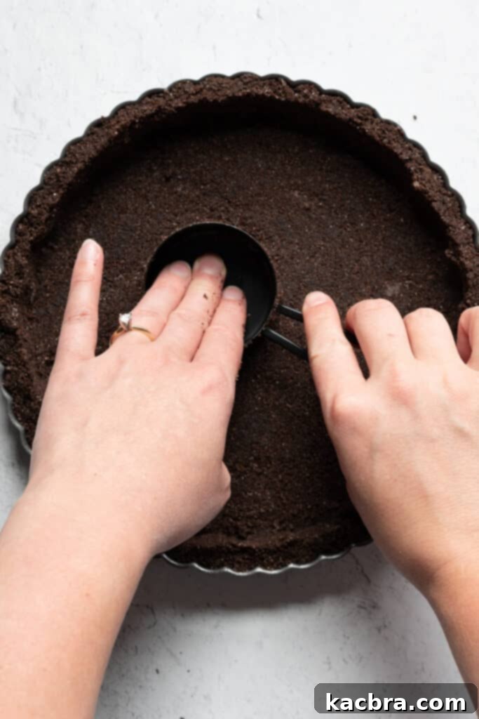The graham cracker crust mixture being pressed into a tart pan with a measuring cup.
