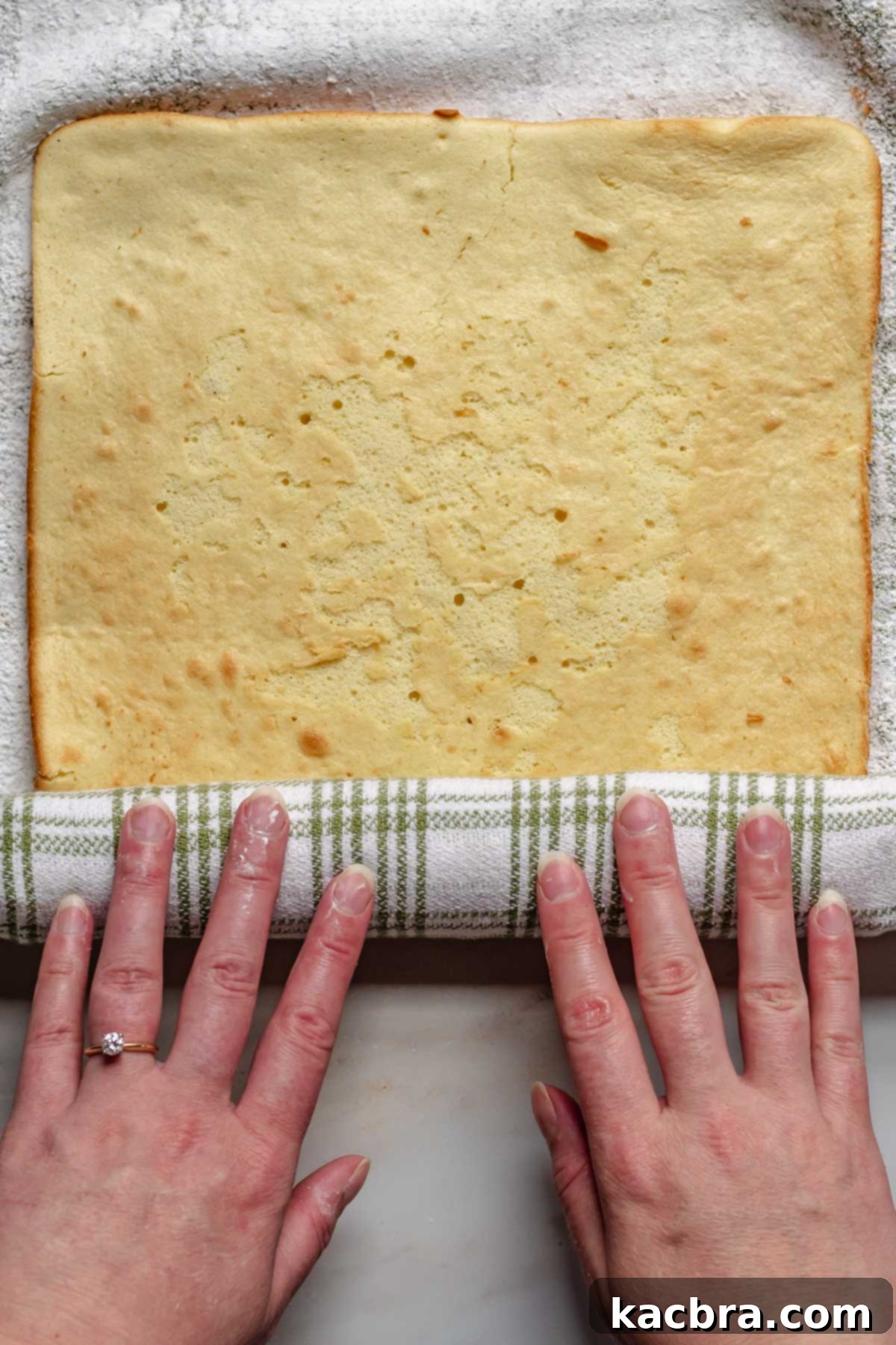 Hands roll up the baked Swiss roll in a kitchen towel.
