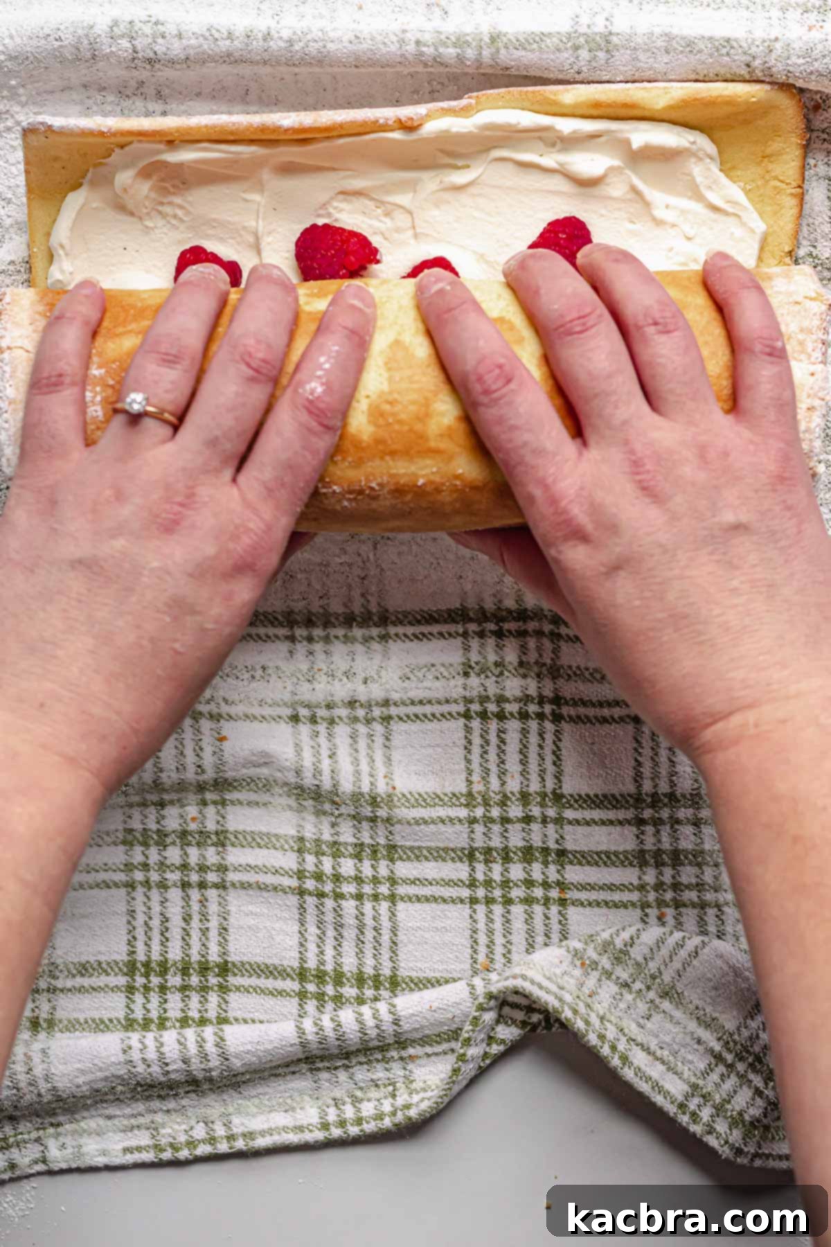 Hands roll up the filled vanilla Swiss roll.