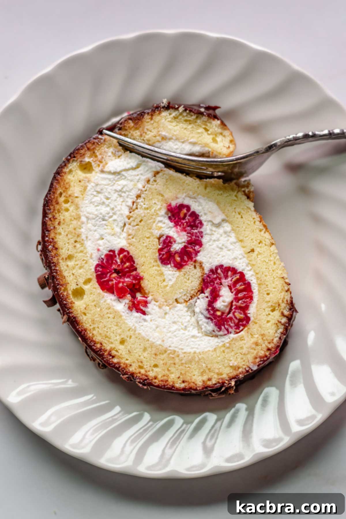 Raspberry and Vanilla Swirl Cake with Decadent Chocolate Ganache 3 Slice of Swiss roll on a plate with a fork removing a piece.