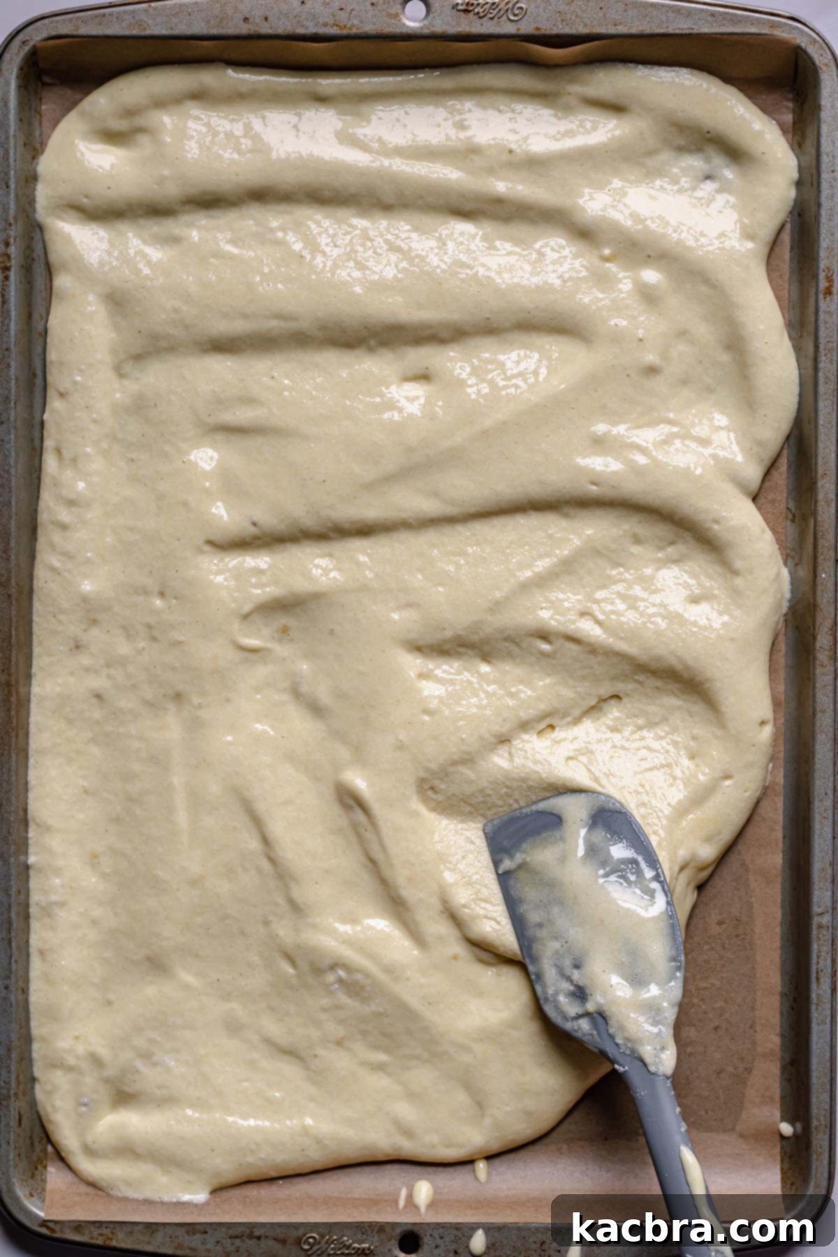 A spatula spreads batter evenly in the pan.