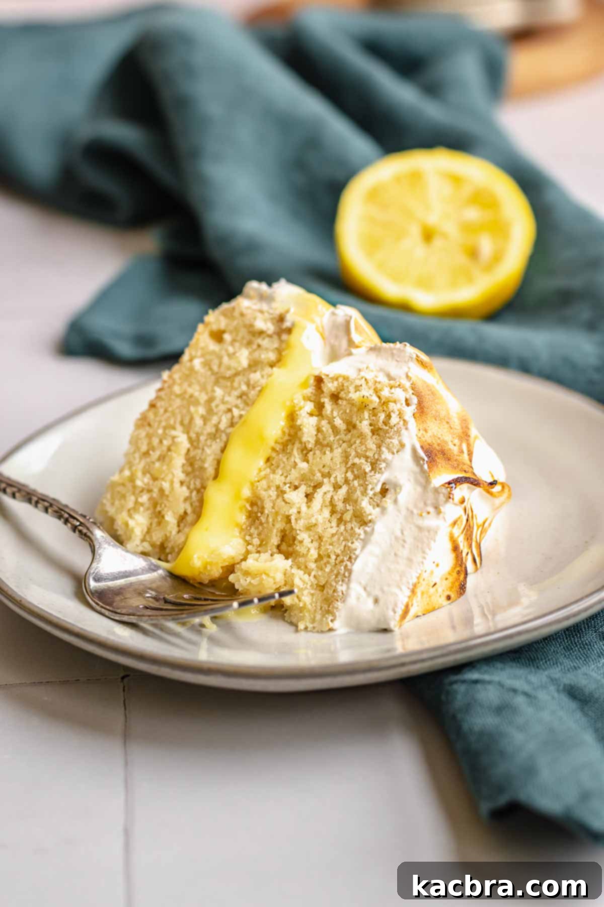 Lemon curd cake slice on a plate with a fork, showcasing the layers.