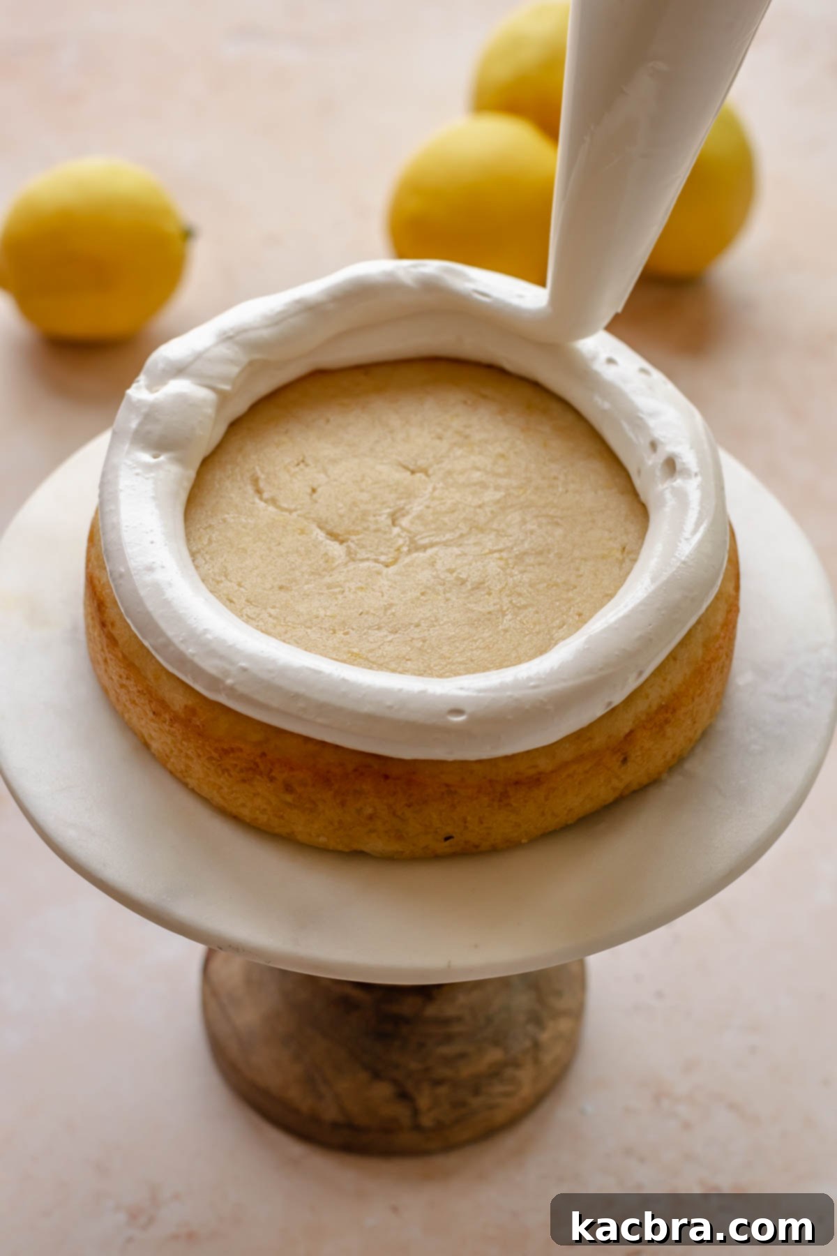 A piping bag pipes Swiss meringue around the edge of one cake layer.