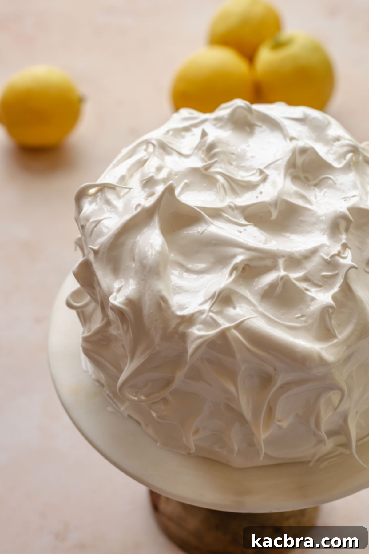 Swiss meringue covered cake with peaks on a cake stand.