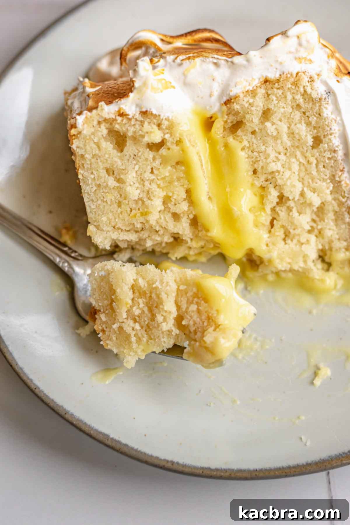 A fork has a piece of lemon meringue cake on a plate, ready to be enjoyed.
