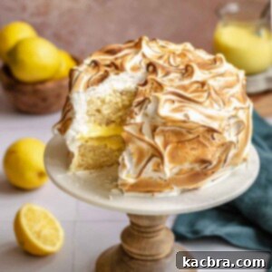 Lemon meringue cake on a stand with a slice removed, revealing its layers.