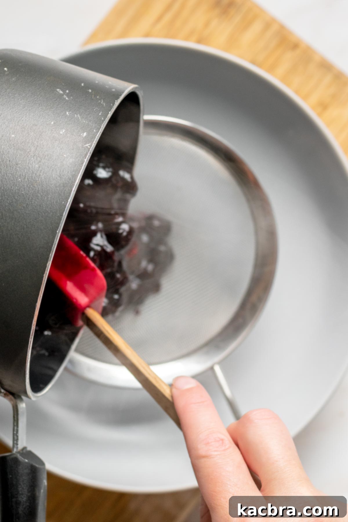 Cooked blueberries being poured through a sieve.
