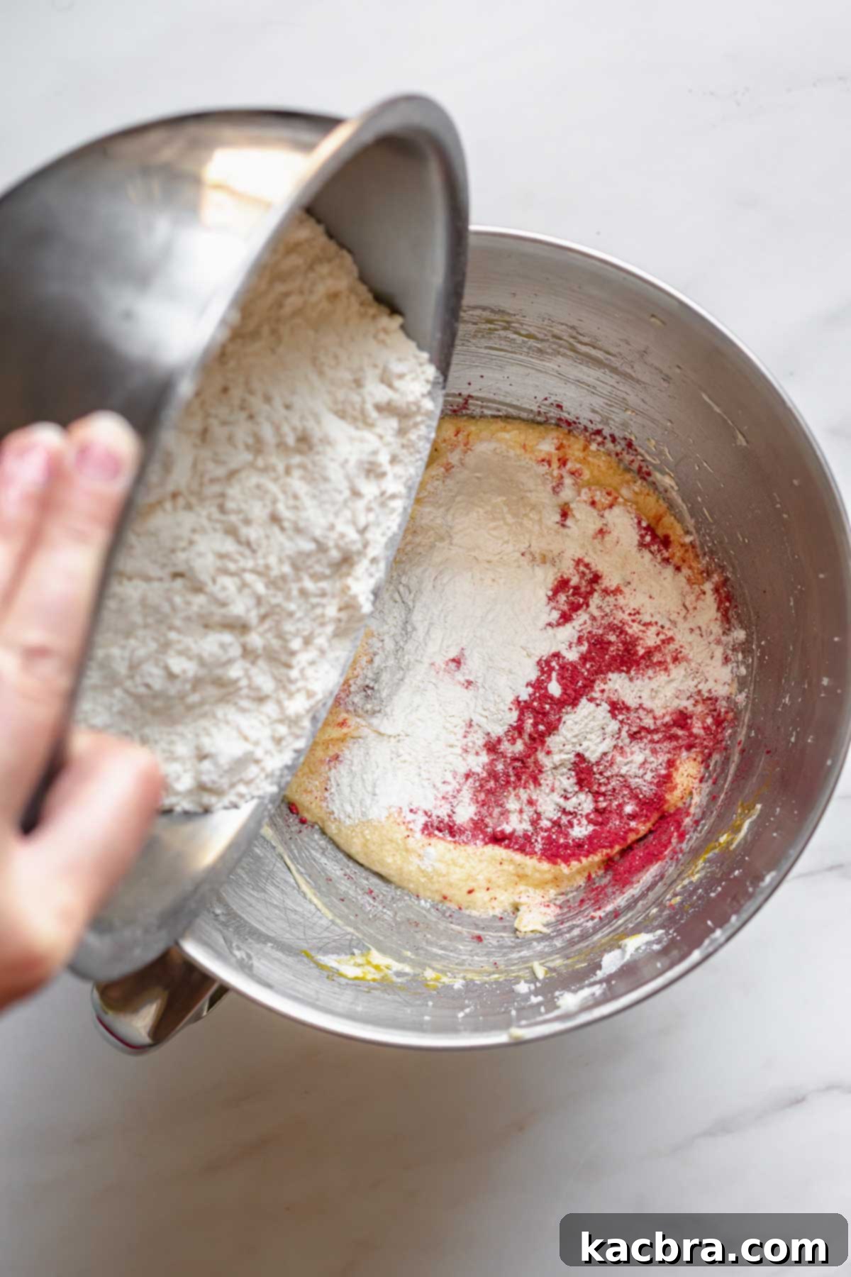 Blushing Strawberry Delights 6 Finely ground freeze-dried strawberry powder and dry ingredients are gently poured into a bowl of creamy vanilla cake batter, ready to be mixed.