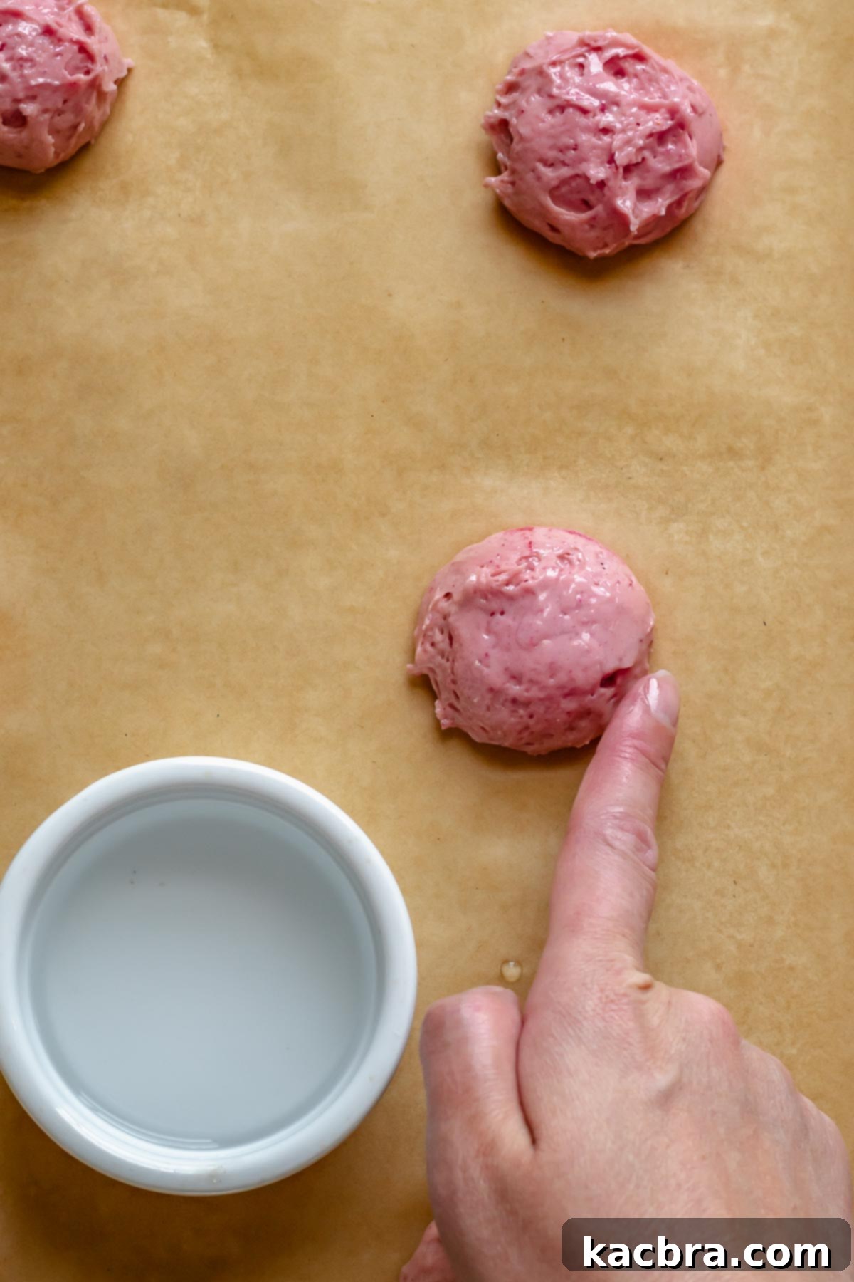 Blushing Strawberry Delights 10 A finger gently dabbing the top of a dollop of cake batter with water to smooth its surface before baking, ensuring a flat whoopie pie.