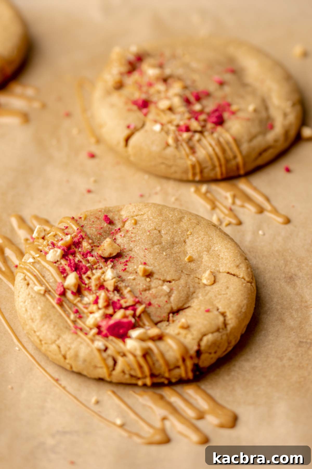 Jammy Peanut Butter Delights 13 Baked peanut butter and jelly cookies on a pan, with melted peanut butter drizzled on top and crushed peanuts.
