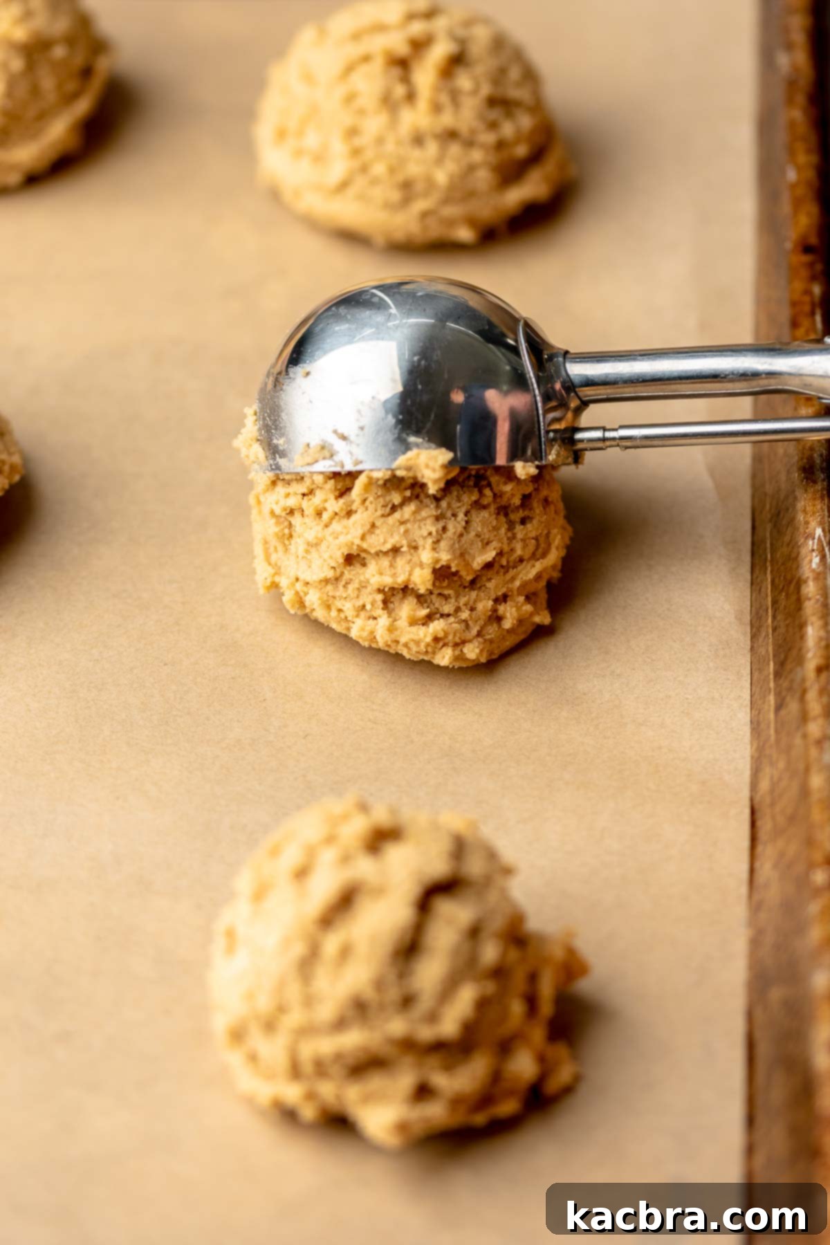 Jammy Peanut Butter Delights 8 A cookie scoop placing balls of peanut butter dough onto a parchment-lined baking sheet.