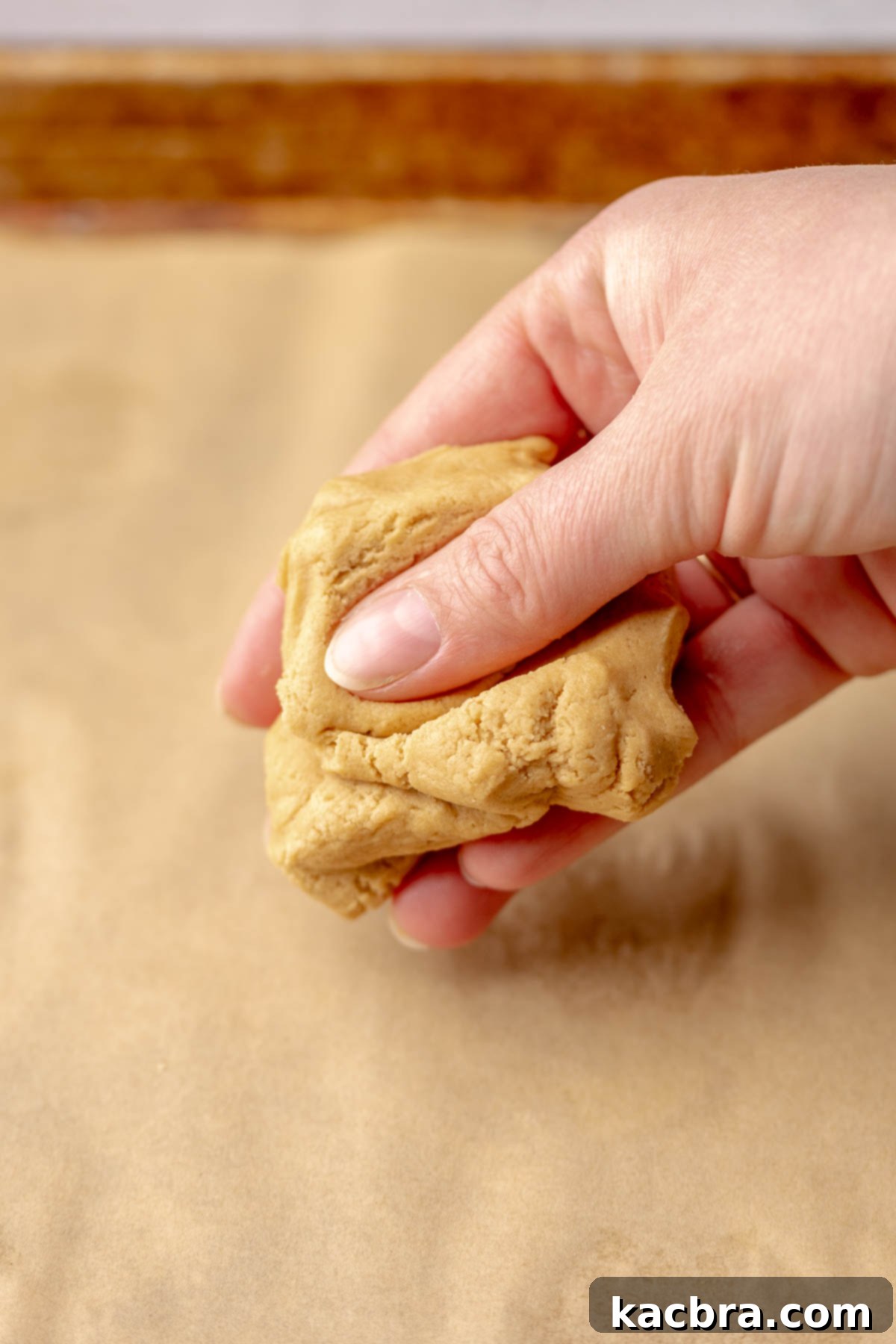 Jammy Peanut Butter Delights 9 A hand gently squishing a ball of peanut butter cookie dough to bring it together.