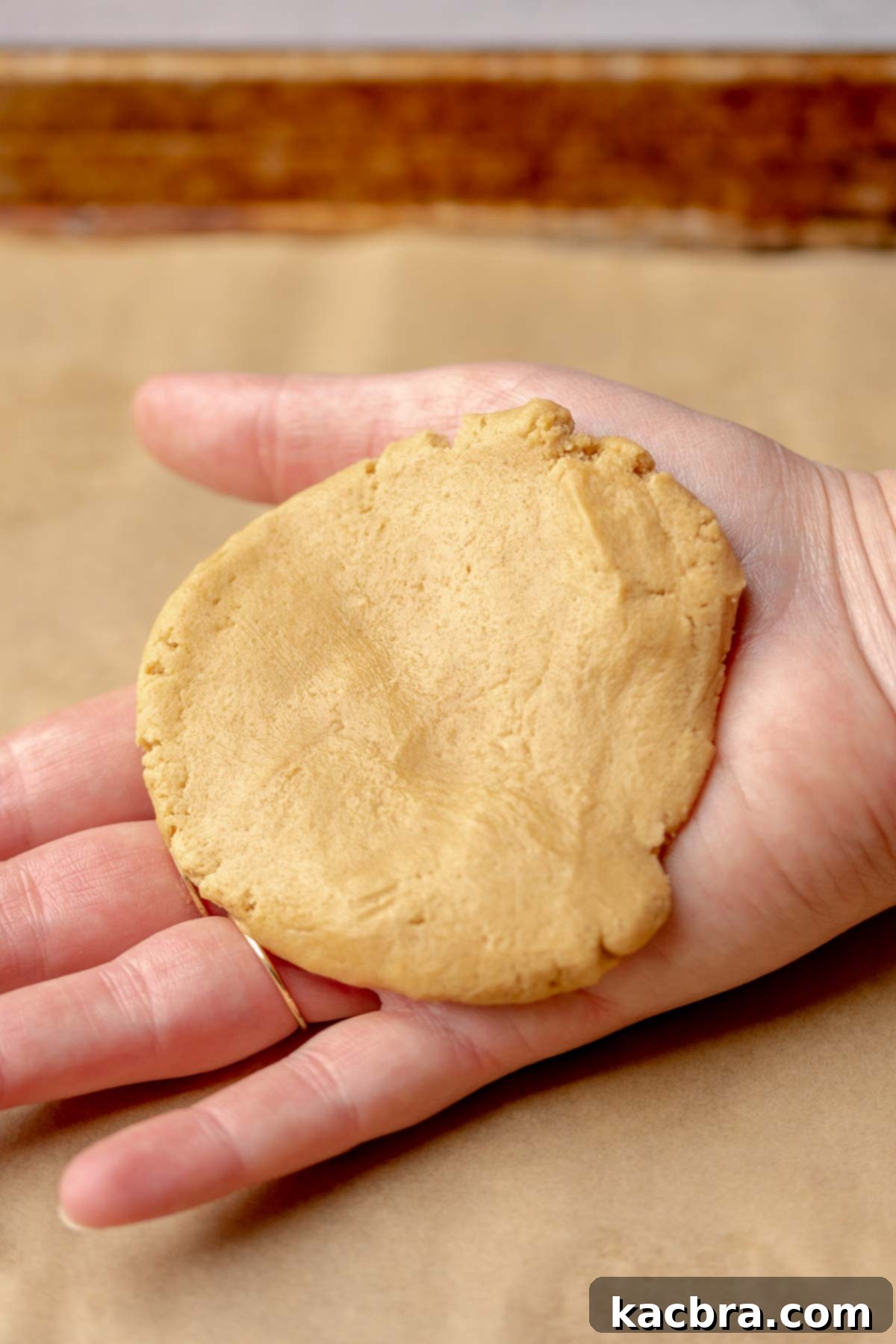 Jammy Peanut Butter Delights 10 A hand holding a flattened piece of peanut butter cookie dough, ready for filling.