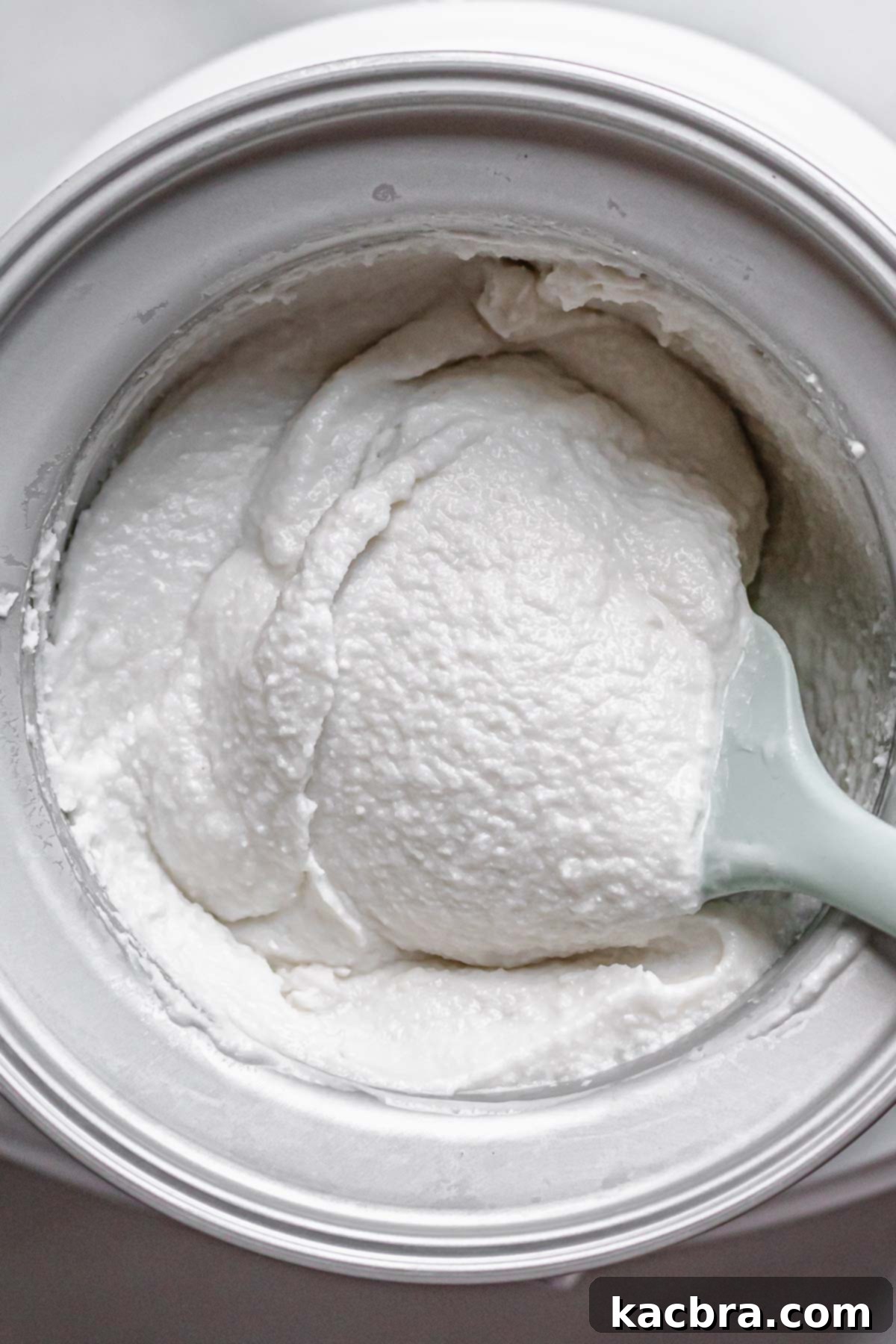A spatula lifts a portion of the churning coconut sorbet, revealing its developing soft-set, creamy texture.