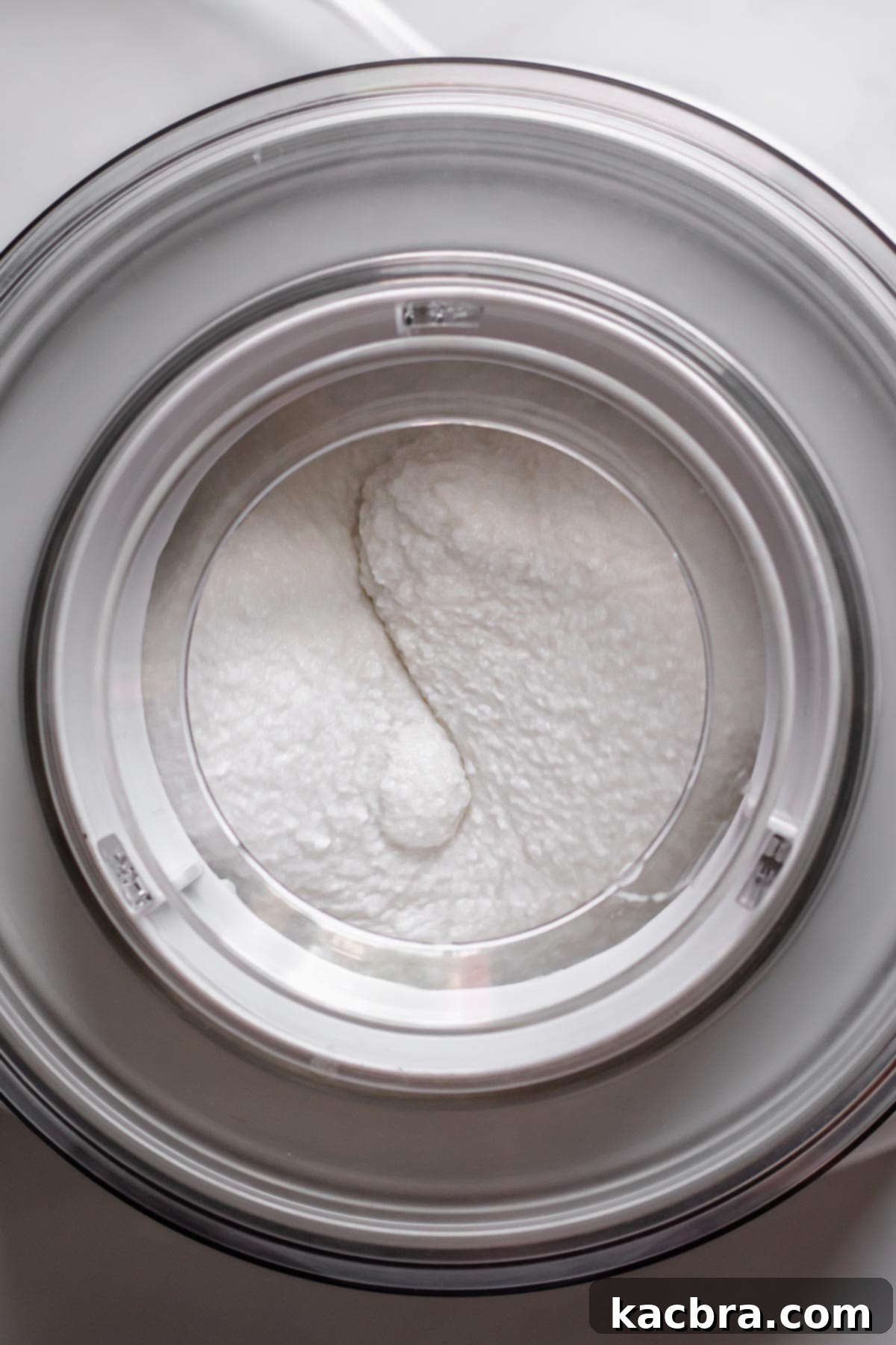 Coconut sorbet actively churning within an ice cream machine, showing its thickening consistency.