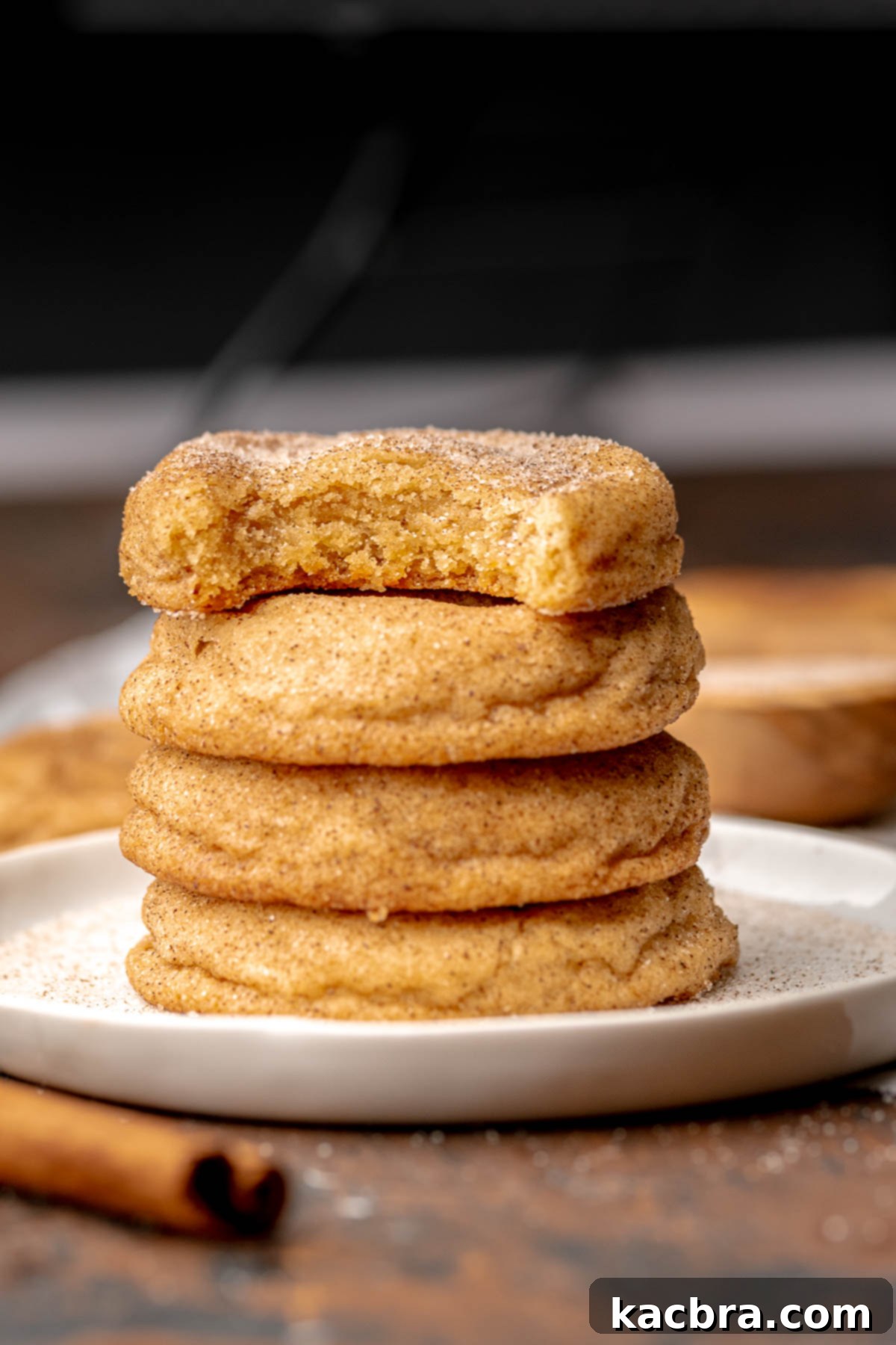 Snickerdoodle cookies stacked on a plate. The top cookie has a bite removed.