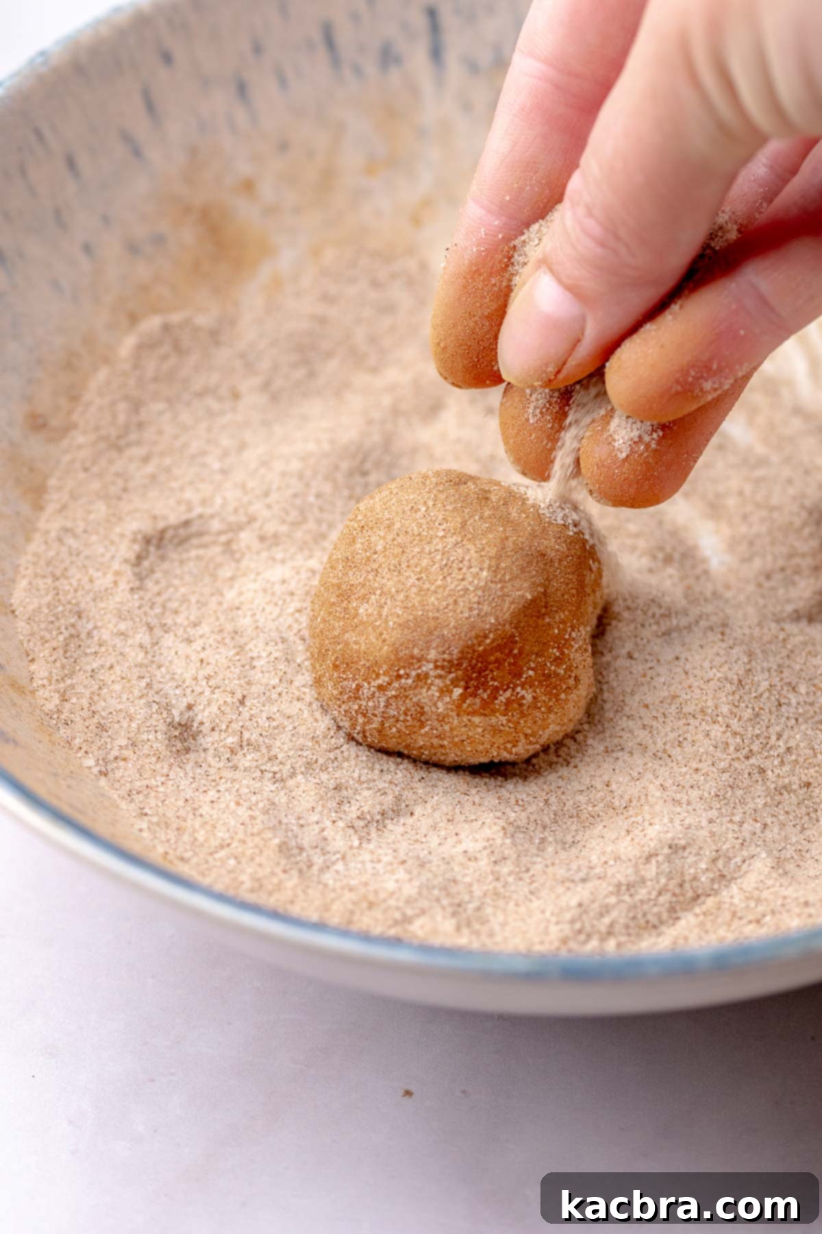 A ball of cookie dough being rolled in cinnamon sugar.