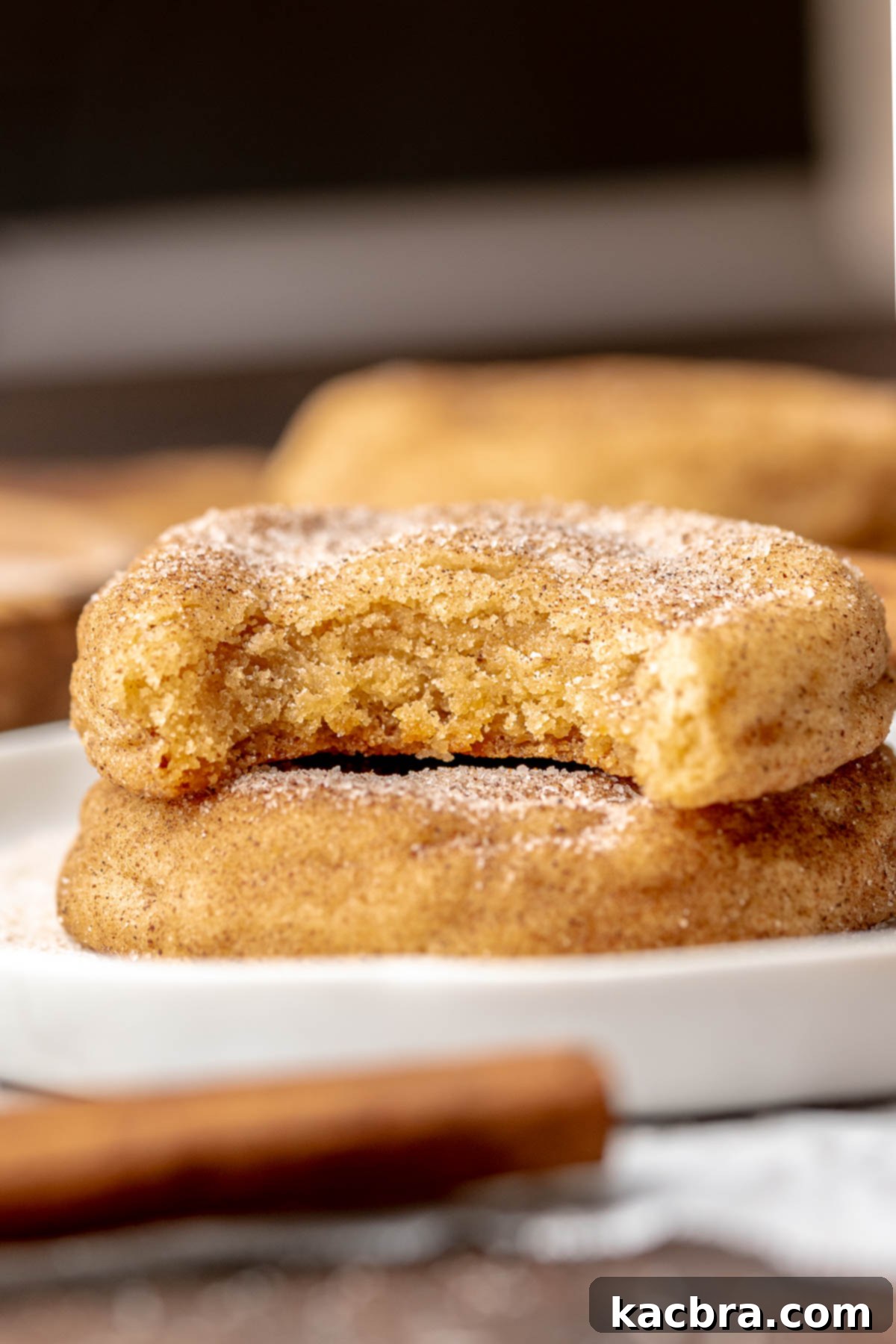 Snickerdoodle cookies stacked on a plate. The top cookie has a bite removed.