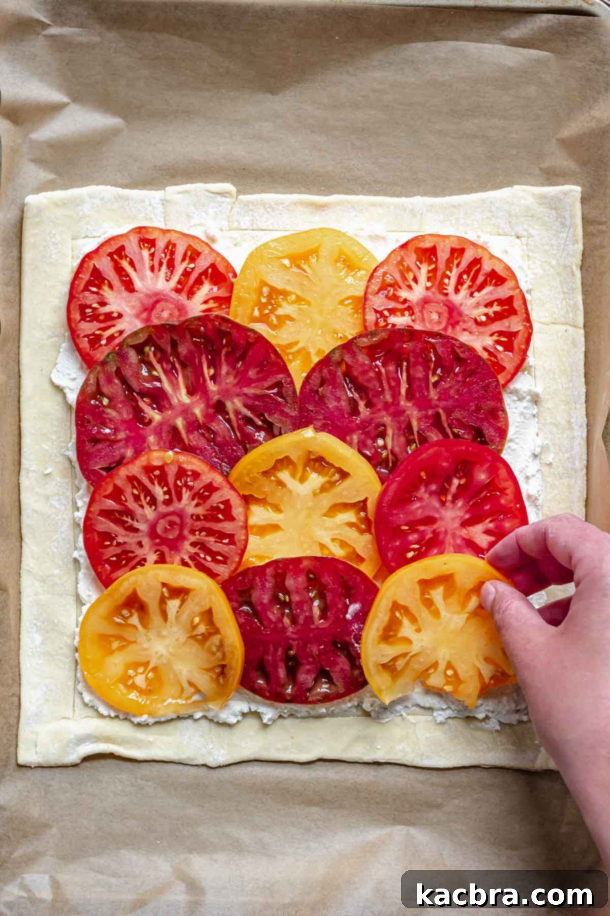 Rustic Tomato and Double Cheese Puff Pastry Tart 6 A hand adds sliced tomatoes on top of the cheese mixture.