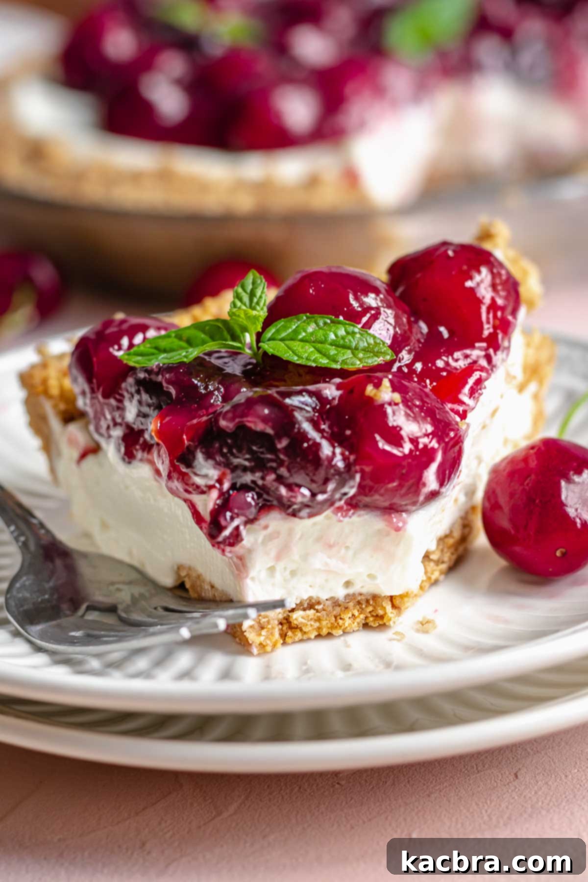 A perfectly sliced piece of no bake cherry cheesecake pie on a white plate with a bite taken out, highlighting its rich layers.