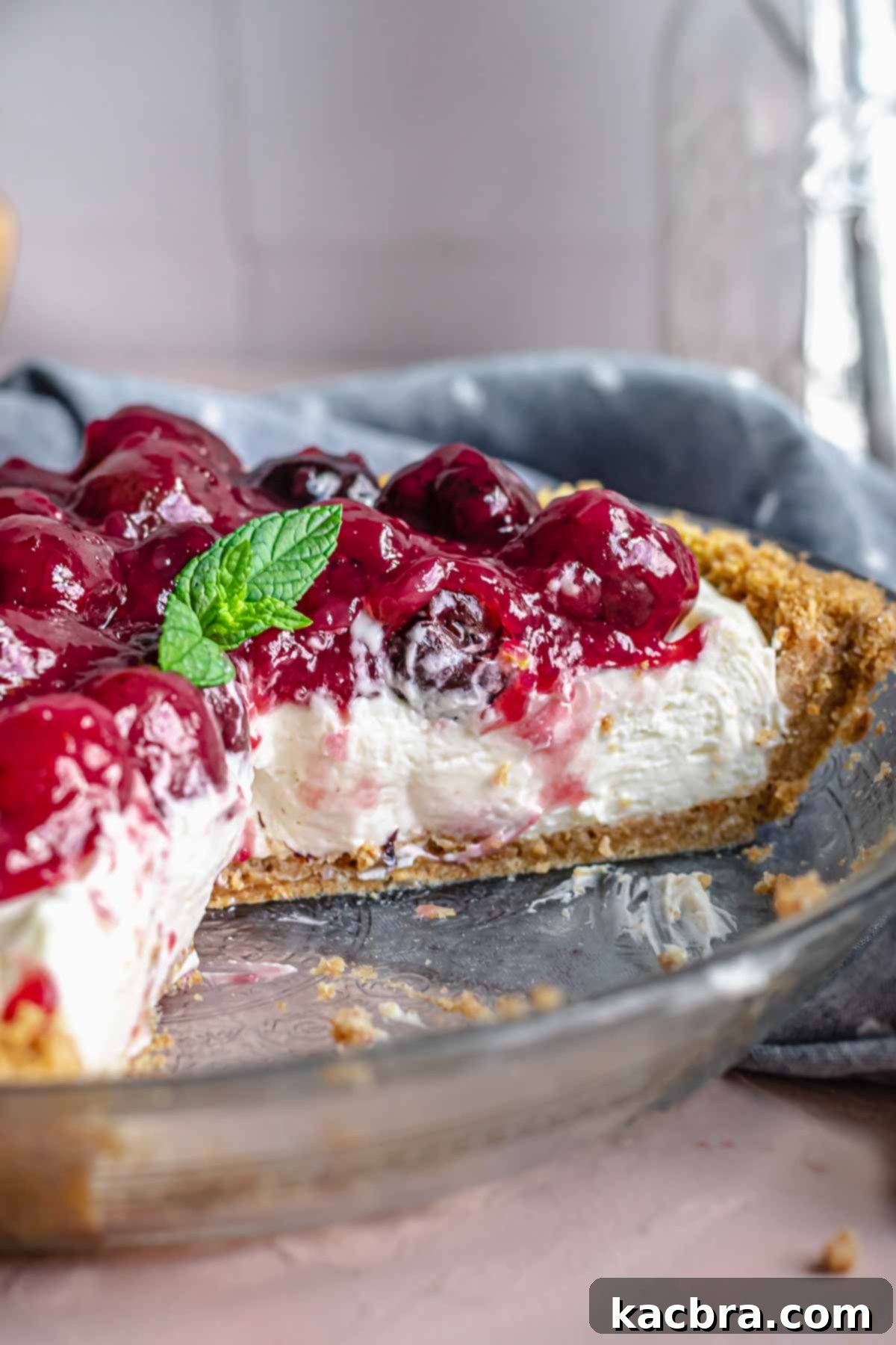 A whole cherry cheesecake pie in a pie dish, with a few slices already removed, showing the creamy interior and thick cherry topping.