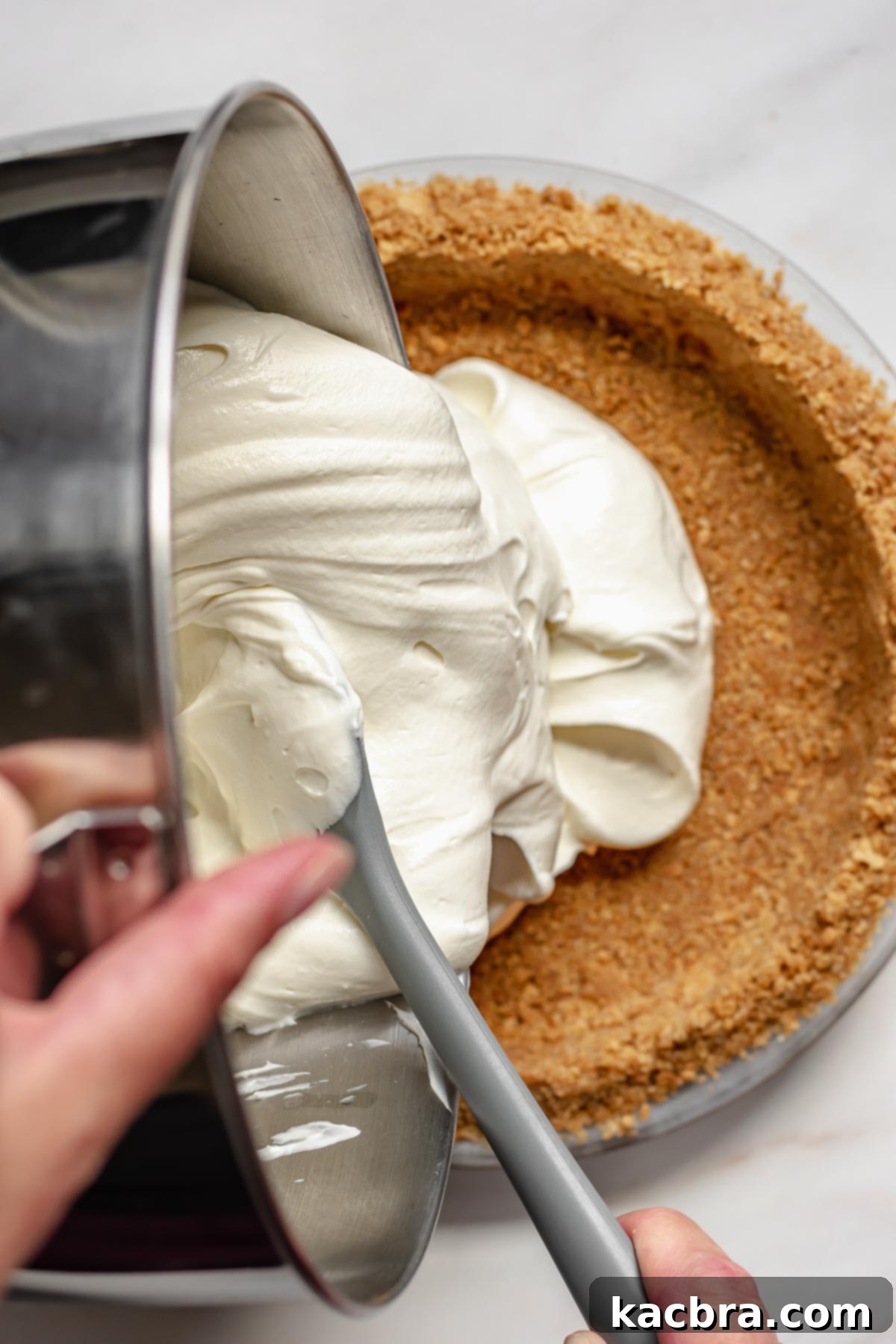 The creamy cheesecake mixture being carefully poured into the chilled graham cracker crust.