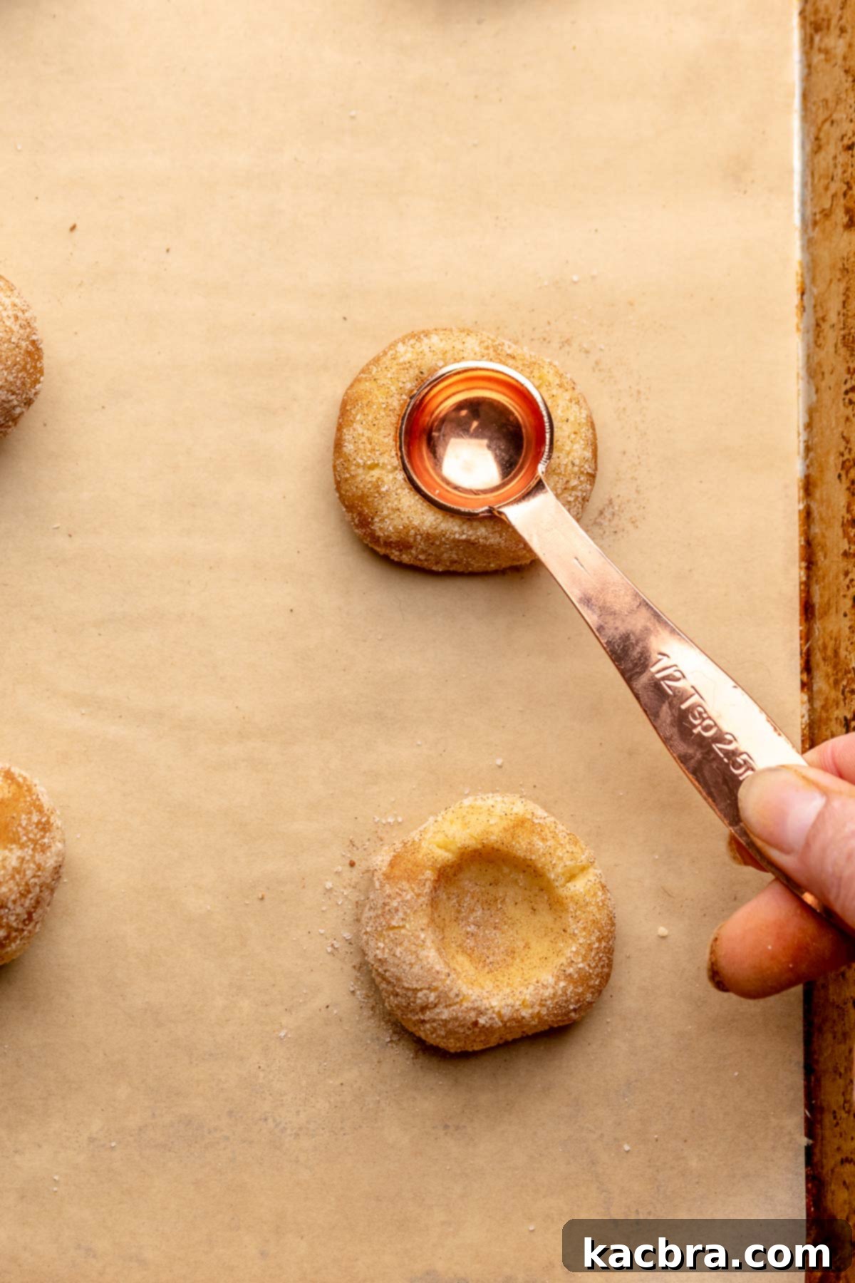 A hand uses a ½ teaspoon measure to press an opening into a dough ball.