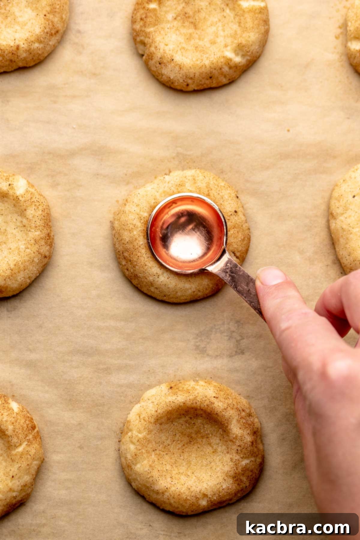A hand uses a 1 teaspoon measure to press an opening into a baked cookie.