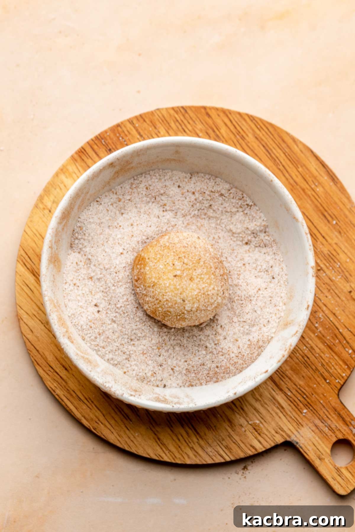 A cookie dough ball in a bowl of cinnamon sugar.