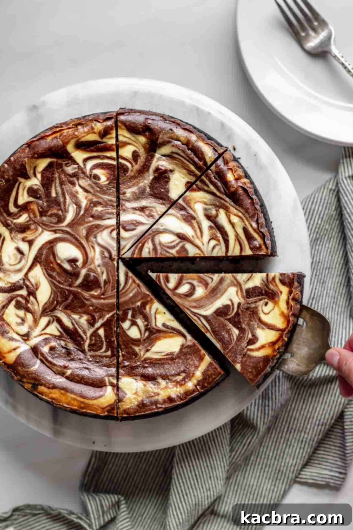 A slice of chocolate marble cheesecake being removed from a platter, showcasing its distinct chocolate and vanilla swirls and dark Oreo crust.