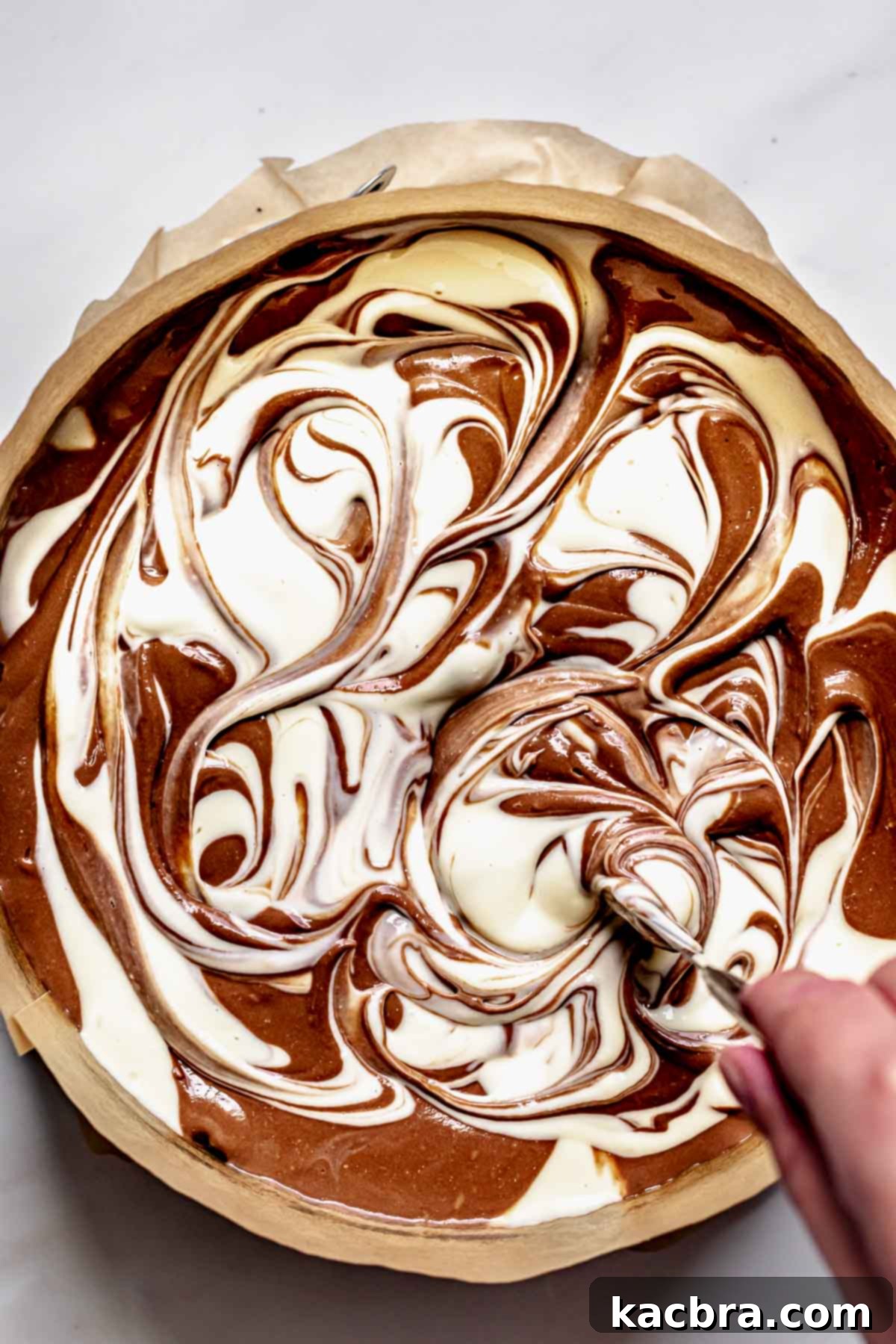 A knife is used to create a beautiful swirl pattern in the combined chocolate and vanilla cheesecake batter.