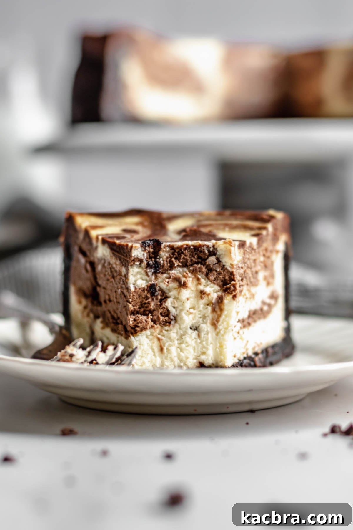 Slice of chocolate marble cheesecake on a plate with a bite removed, showing the creamy interior and swirled pattern.