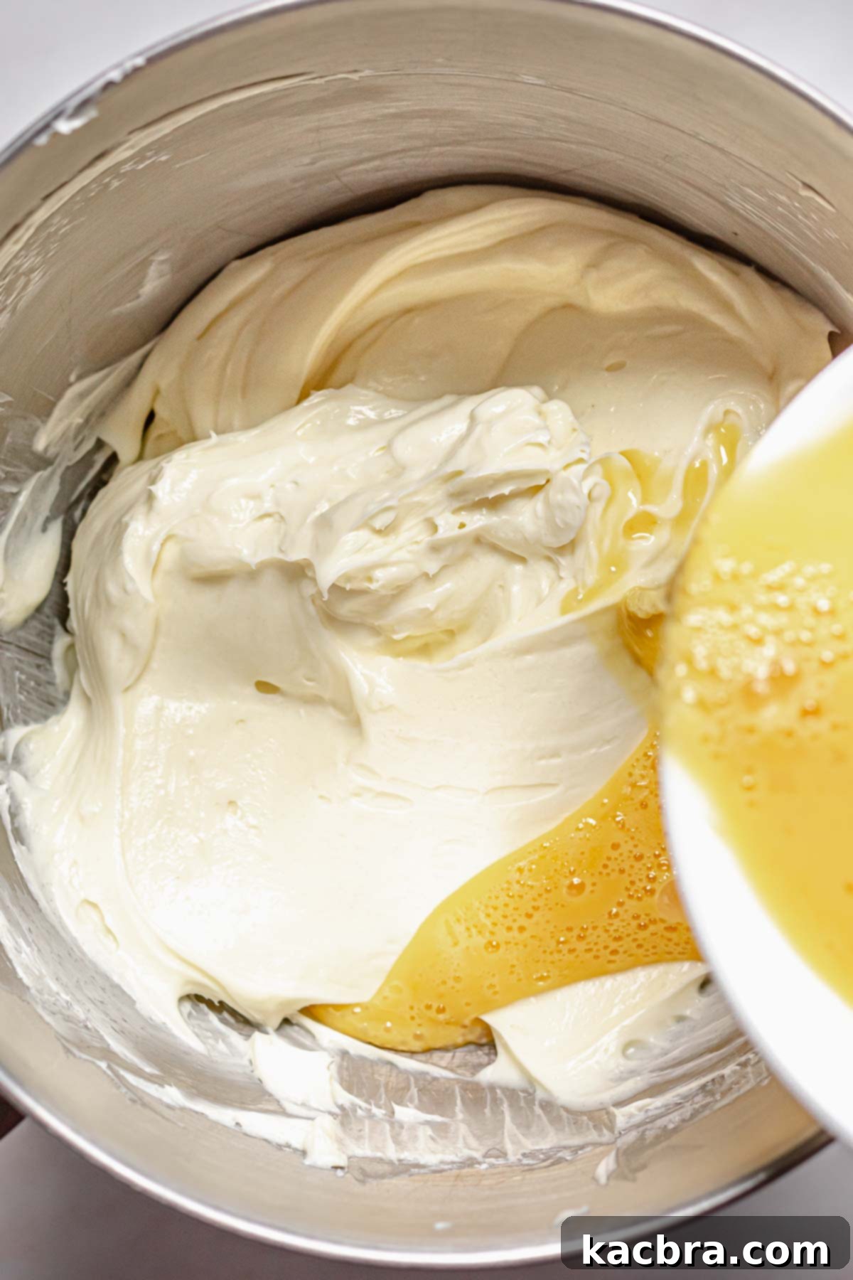 Adding lightly whisked eggs into cheesecake batter on low speed.