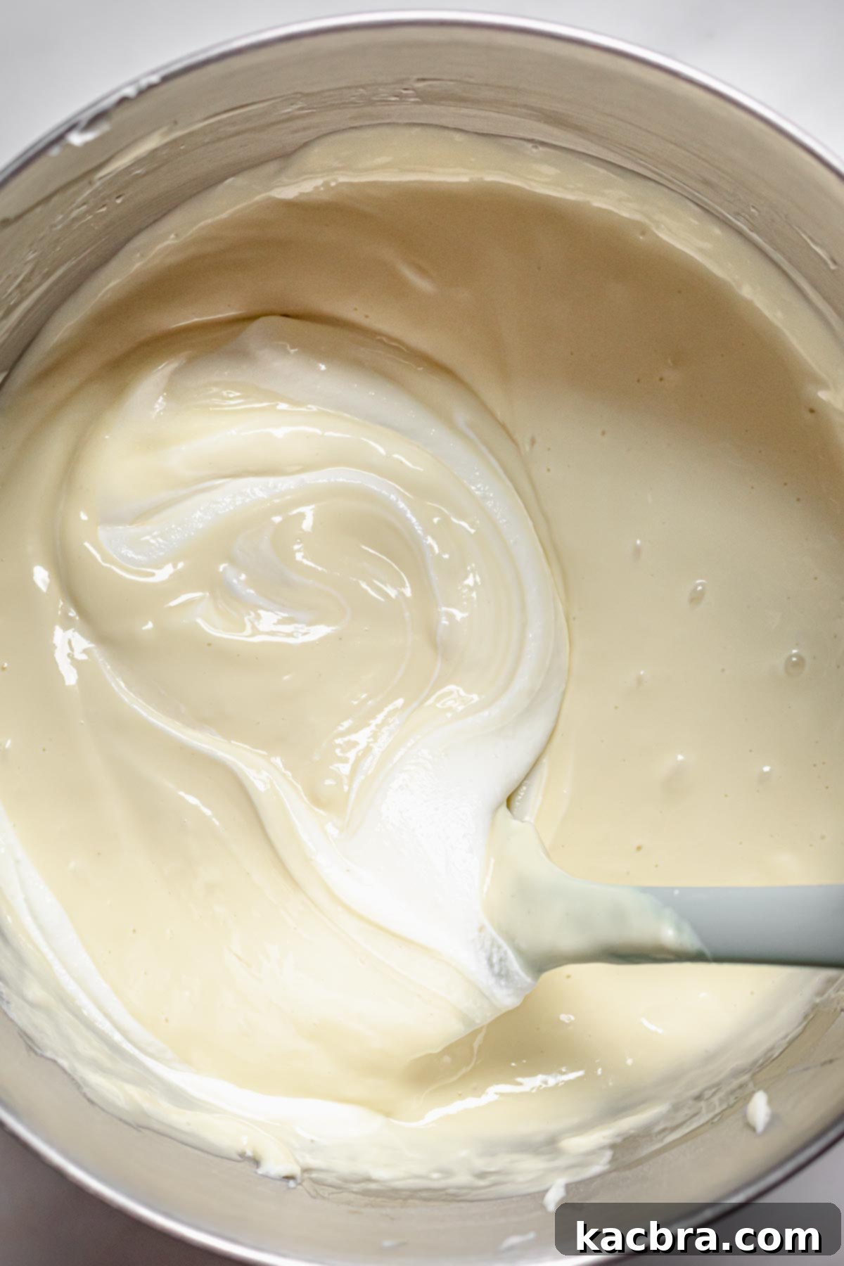 A rubber spatula gently folds sour cream into the cheesecake batter until fully combined.
