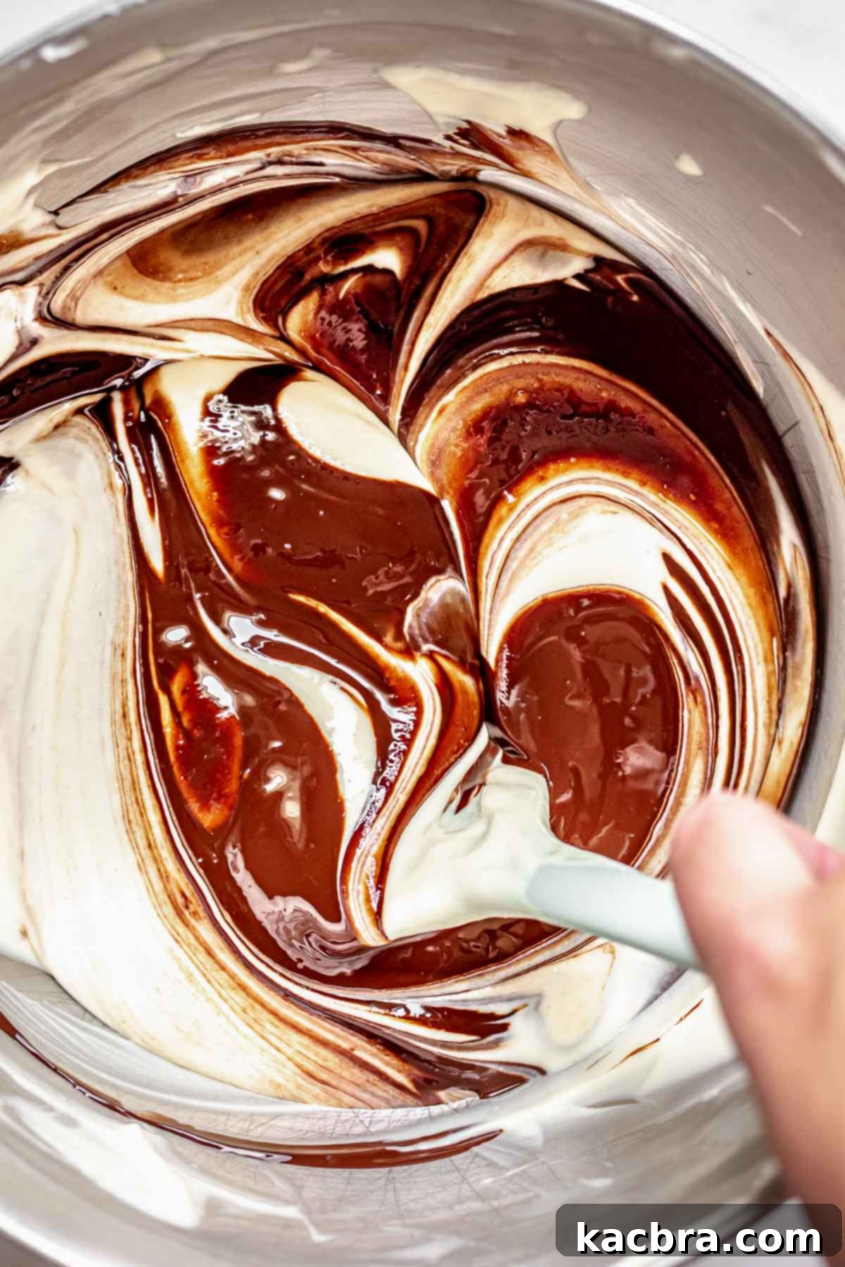 A spatula gently folds melted chocolate into the cheesecake batter until it's a smooth, rich chocolate mixture.