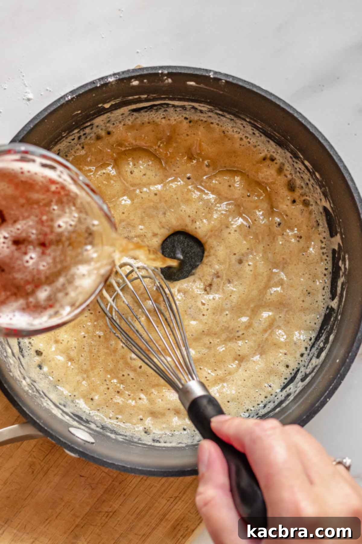 Beer being whisked into a roux in a pot.