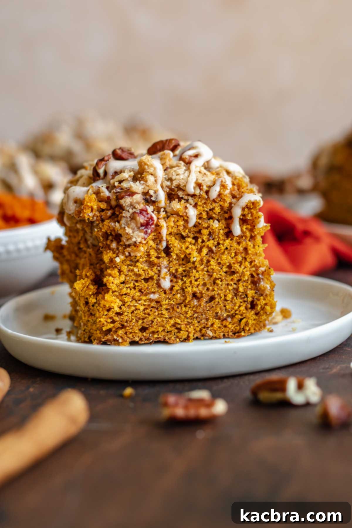 A perfectly sliced piece of pumpkin coffee cake, showing its layers and crumb topping, resting on a white plate.