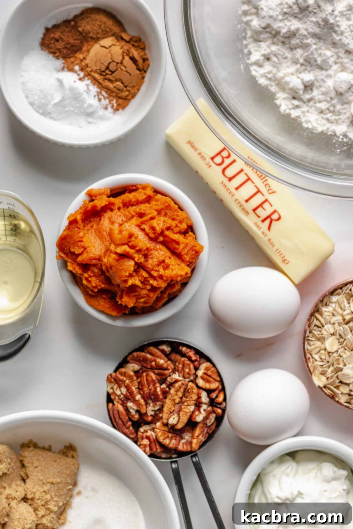 All the ingredients for pumpkin pecan coffee cake laid out on a table, including spices, flour, butter, oil, pumpkin puree, eggs, oats, pecans, brown sugar, white sugar, and sour cream.