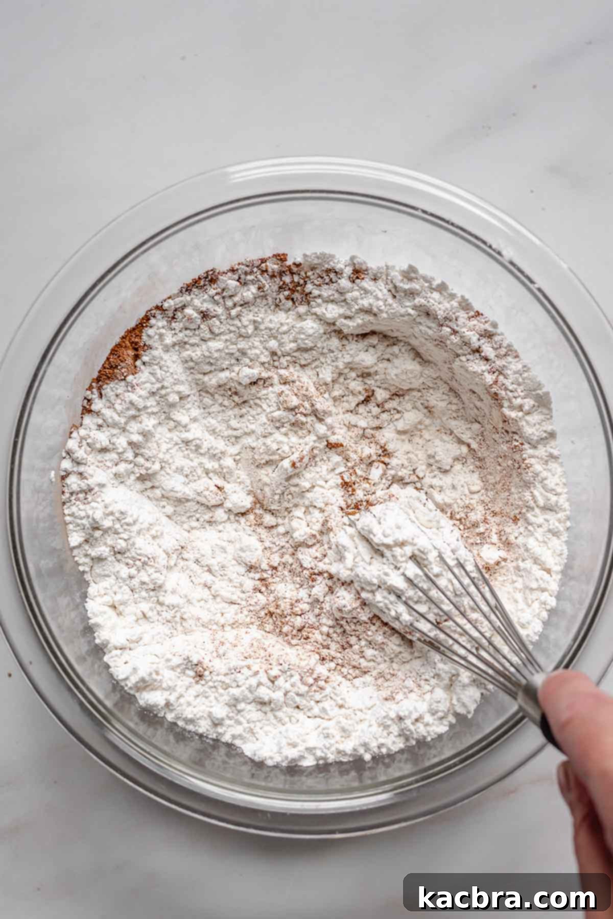 Whisking dry ingredients like flour, baking powder, and spices in a medium bowl.