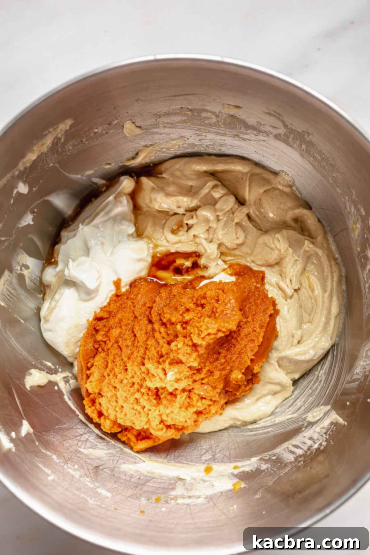 Pumpkin puree and sour cream being added to the creamed butter, sugar, and egg mixture in a large mixing bowl.