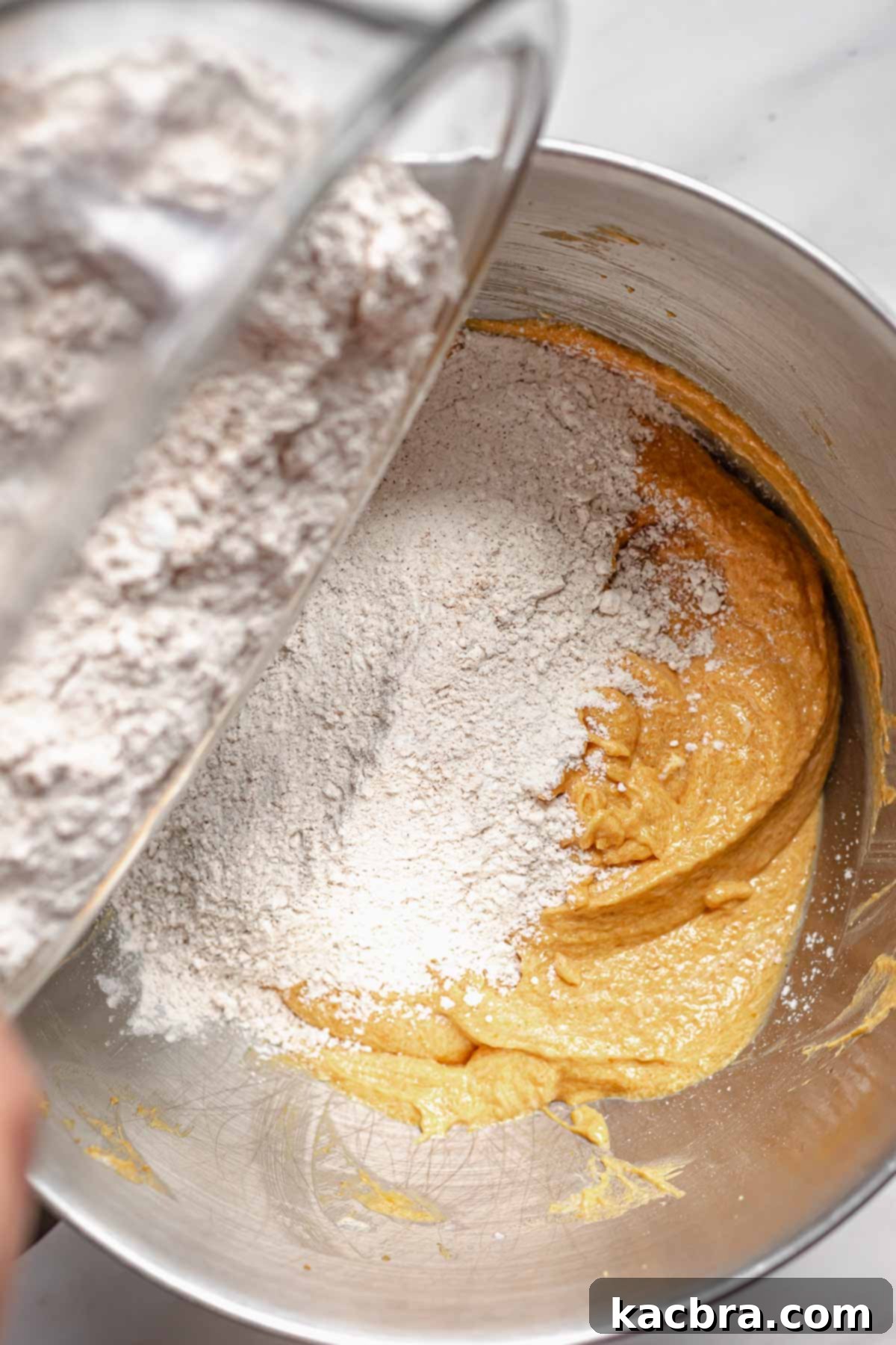 The sifted flour mixture being gently added to the wet batter in a mixing bowl.