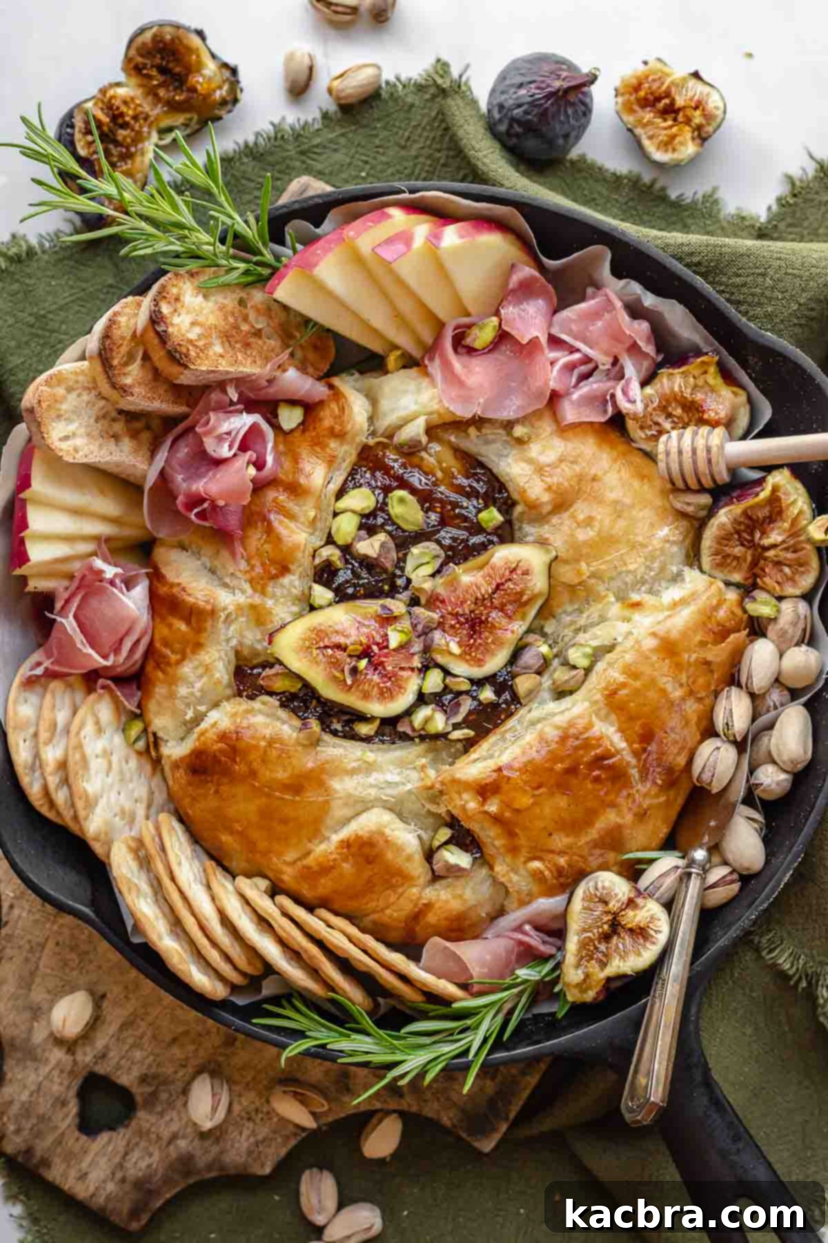 Finished baked brie in a cast iron skillet, surrounded by an assortment of delicious dippers like bread, fruit, and charcuterie.