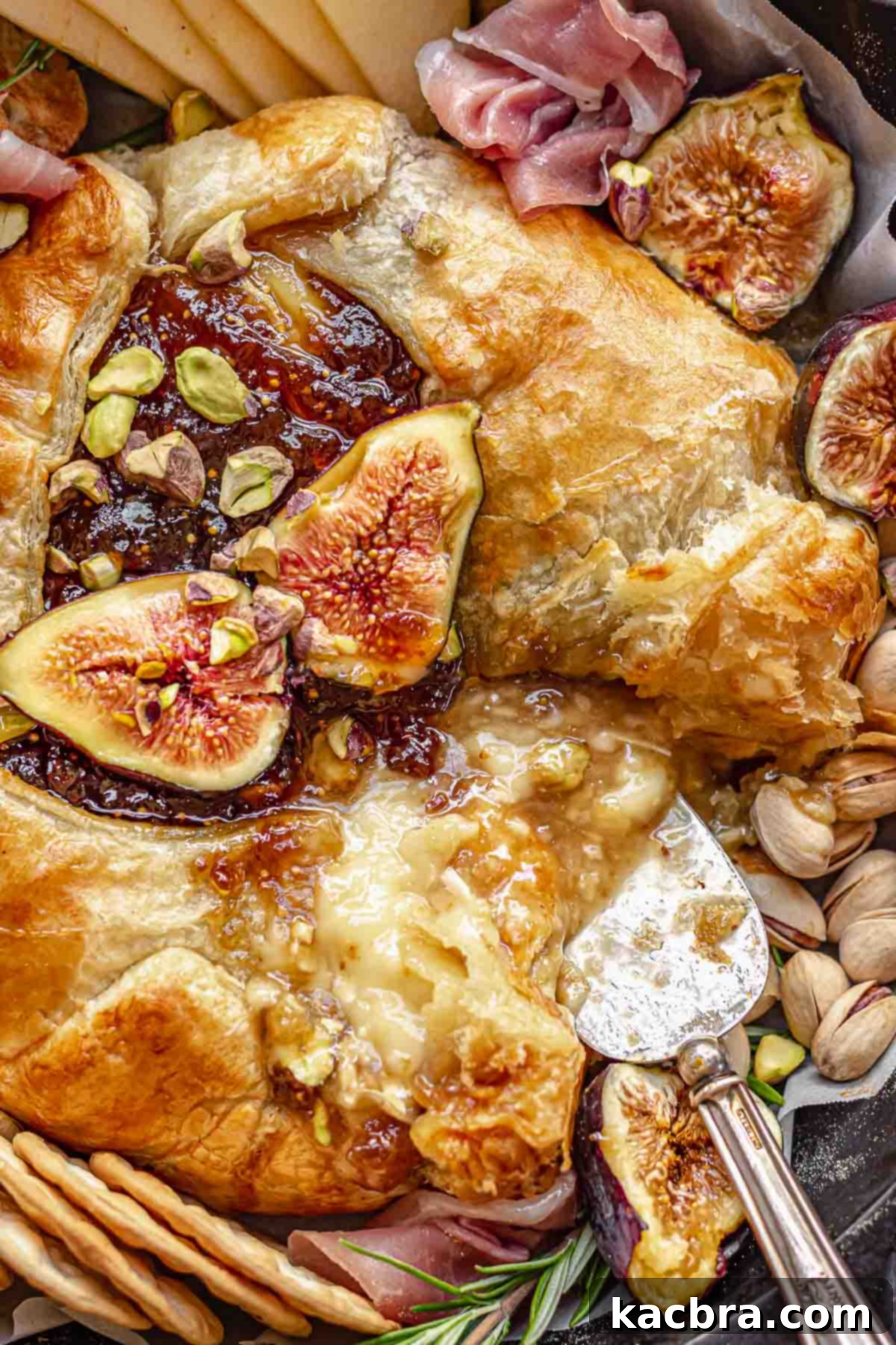 A close-up shot of baked brie with fig jam, with a piece being carefully removed, showing the gooey interior.