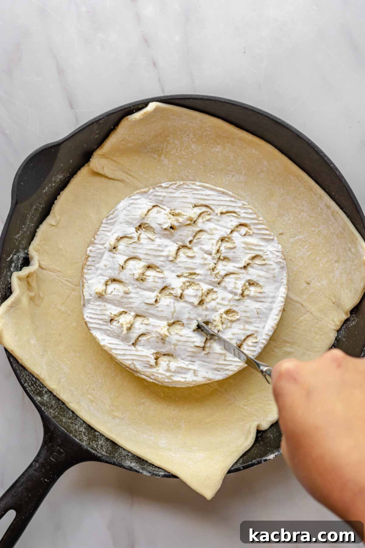 A wheel of brie placed on puff pastry, with a butter knife scoring the rind.