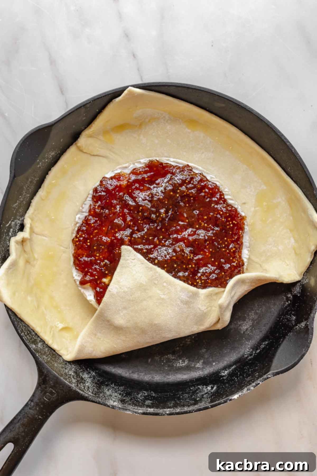 A corner of puff pastry being folded upwards over the brie and fig jam.